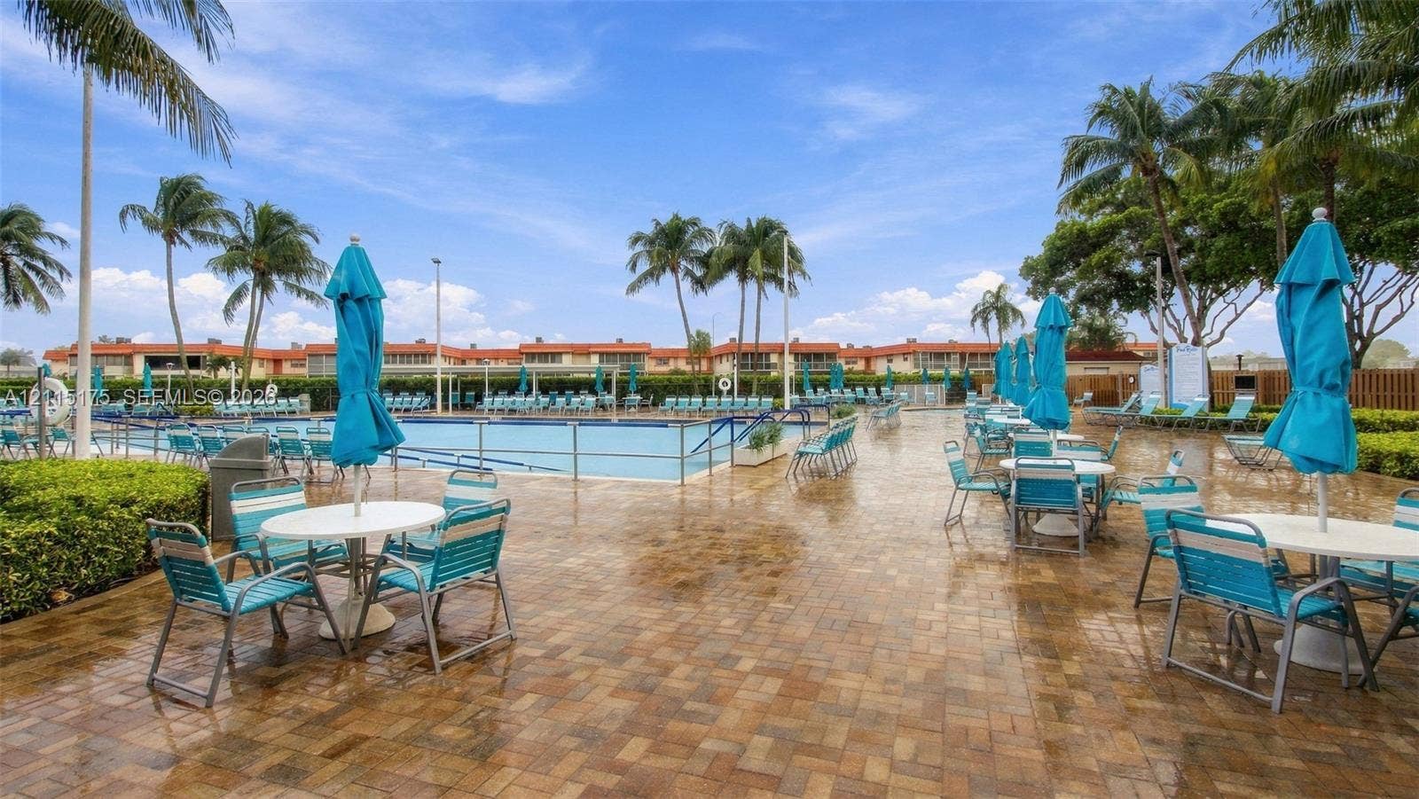 324 Seville N, Delray Beach, FL 33446 Swimming pool area at one of the satellite clubhouses with paver patio, metal perimeter fencing, and mature palm trees