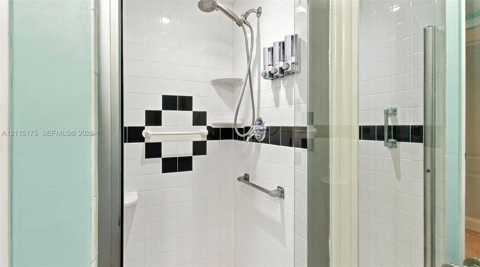324 Seville N, Delray Beach, FL 33446 Primary bathroom walk-in shower enclosure featuring white tile, a black accent tile border, built-in corner shelving and a glass door