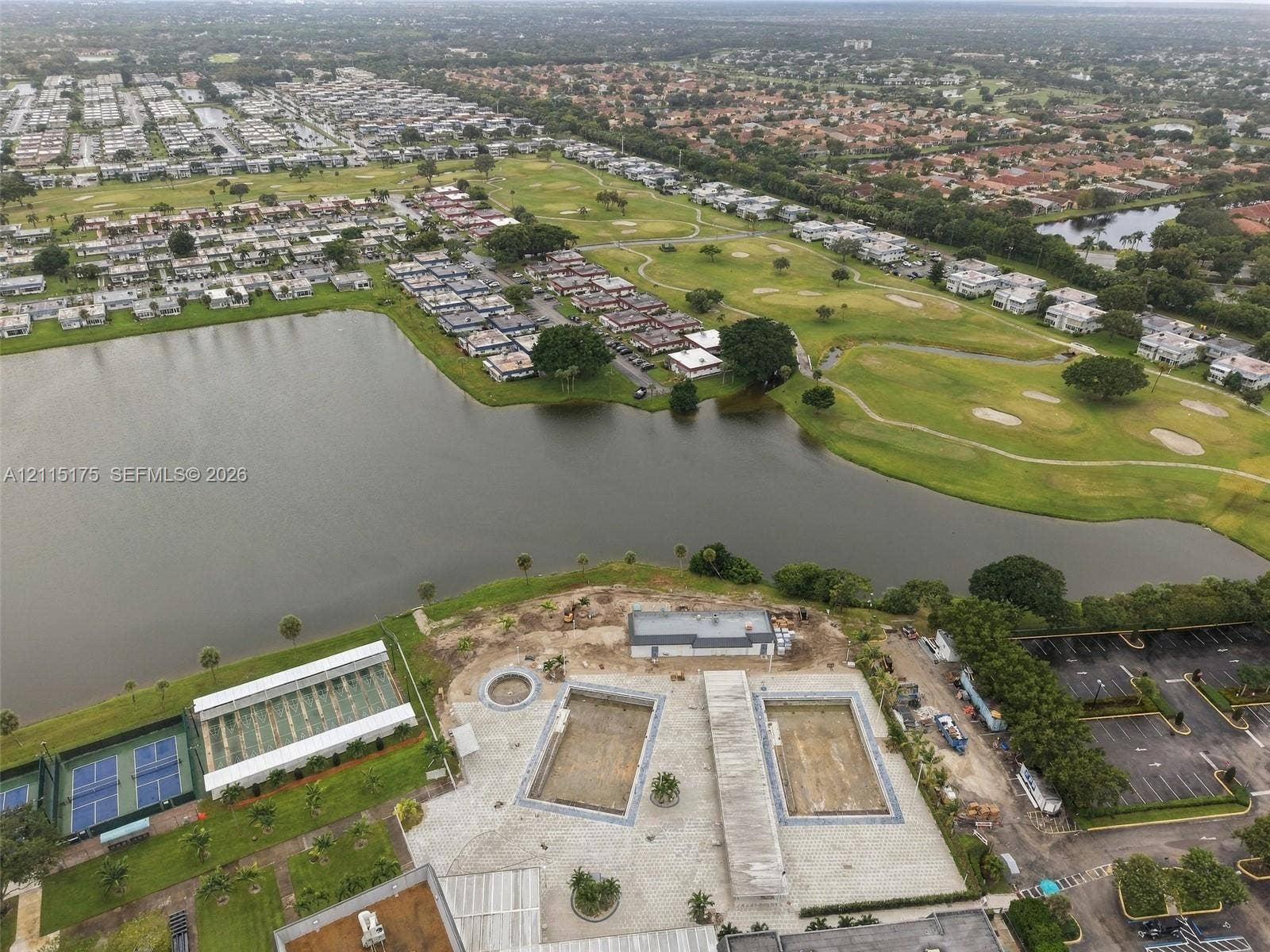 324 Seville N, Delray Beach, FL 33446 Aerial perspective of the community facilities, featuring two rectangular swimming pools, a dedicated tennis court structure, paved parking area, and waterfront positioning