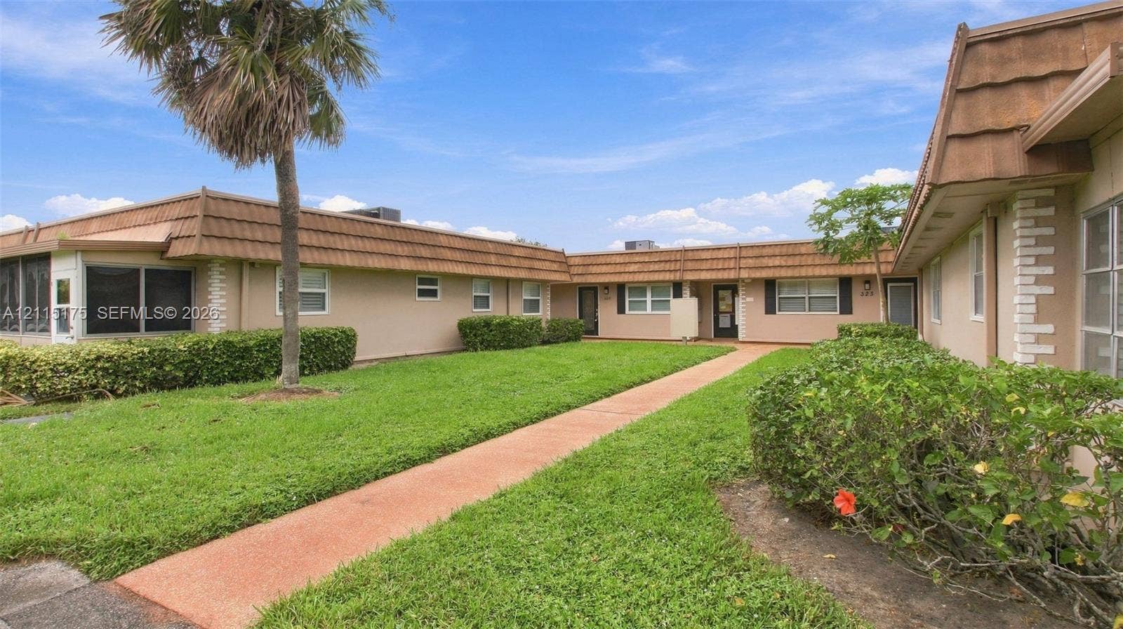 324 Seville N, Delray Beach, FL 33446 Single-story exterior featuring stucco siding, manicured hedges, mature palm trees, and a concrete walkway