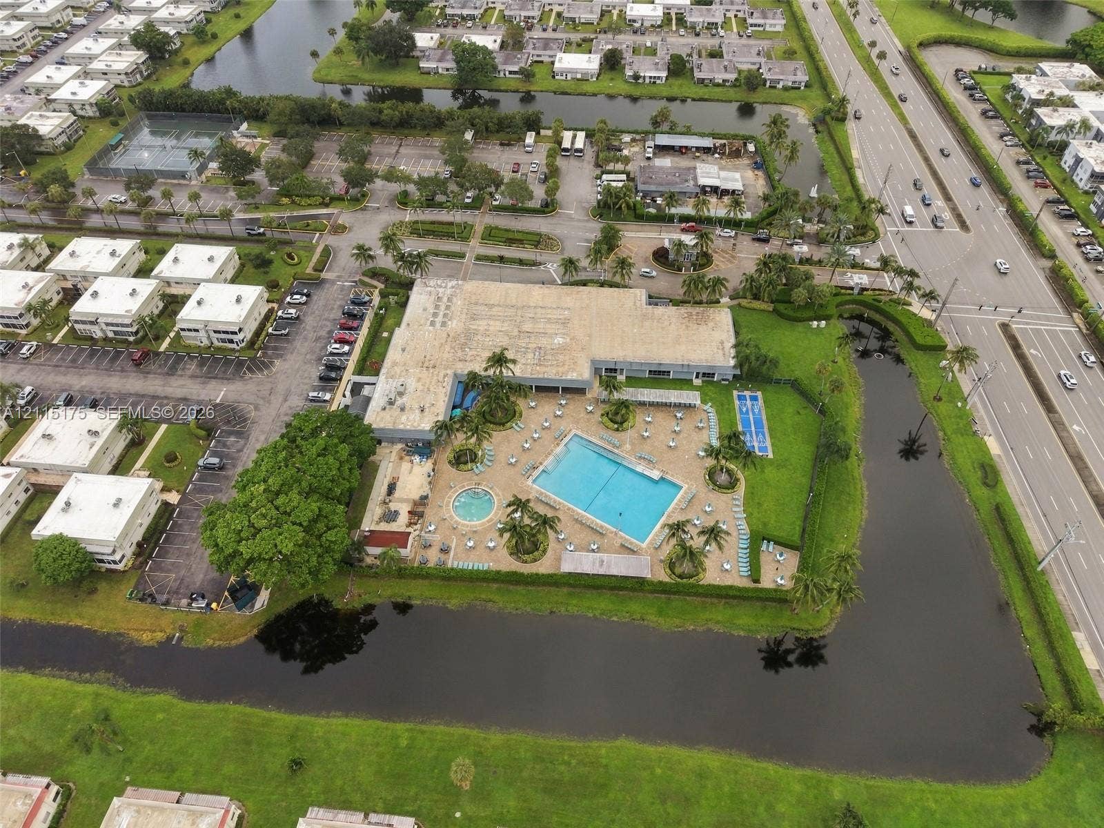 324 Seville N, Delray Beach, FL 33446 Aerial perspective of community facilities featuring a swimming pool, spa, surrounding paved patio, dedicated sports court, and perimeter canal