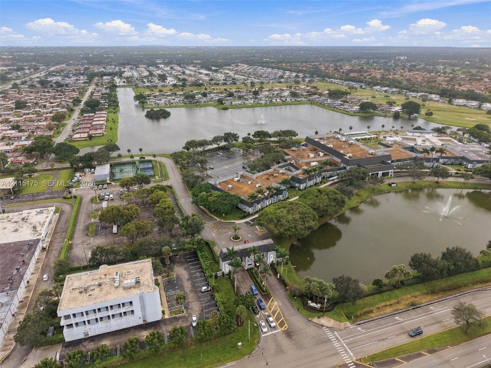 324 Seville N, Delray Beach, FL 33446 Aerial perspective of a multi-structure property featuring expansive water frontage, multiple decorative fountains, tennis courts, and landscaped grounds