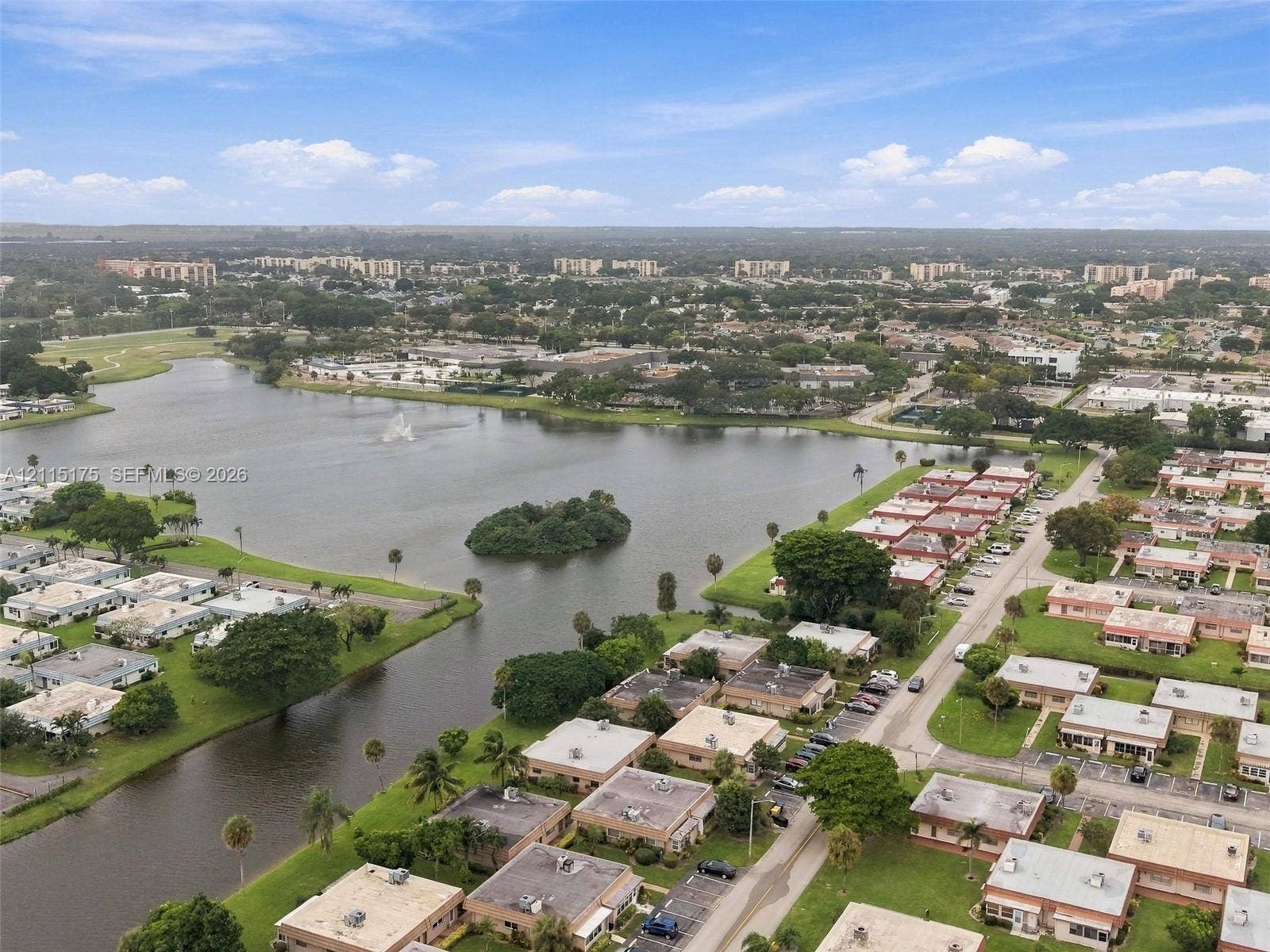 324 Seville N, Delray Beach, FL 33446 Aerial perspective of a multi-unit residential community featuring a large central lake, manicured green space, and mature palm trees