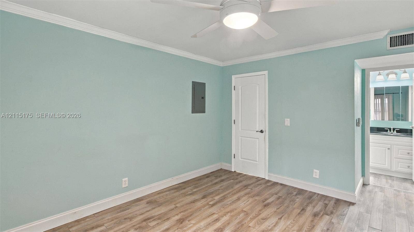 324 Seville N, Delray Beach, FL 33446 Primary bedroom featuring laminate flooring, crown molding, a ceiling fan with integrated lighting, and a solid-core interior door to a walk-in closet