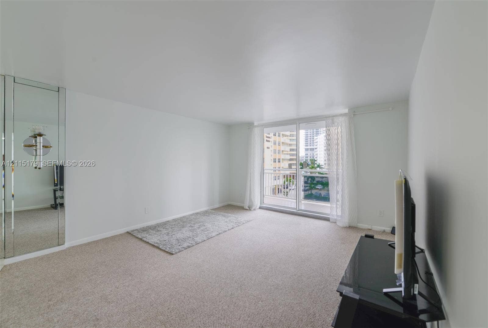 1849 S Ocean Drive, #407, Hallandale Beach, Hallandale Beach, FL 33009 Living area featuring wall-to-wall carpeting, floor-to-ceiling mirrored wall panels, and a sliding glass door providing access to a private balcony