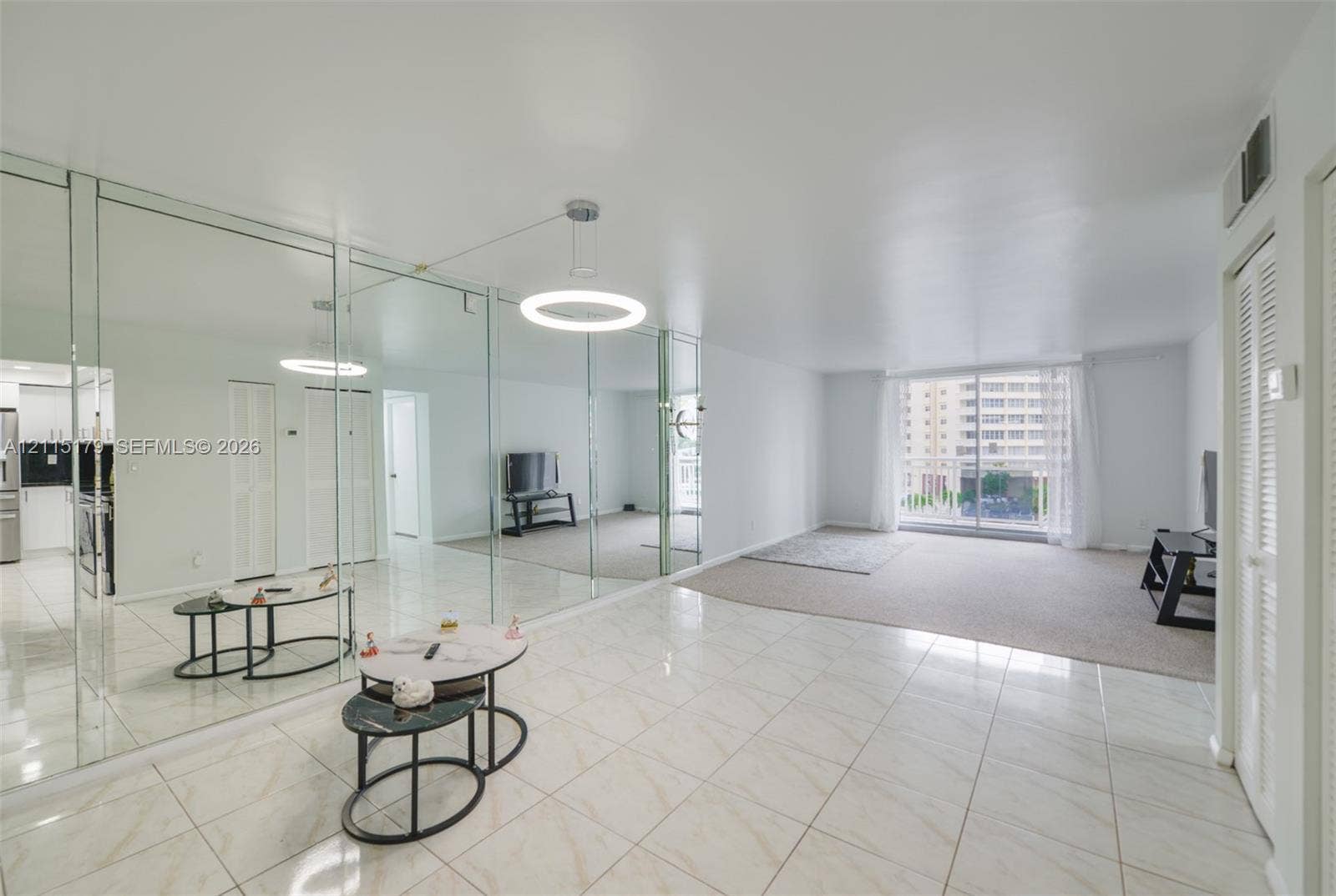 1849 S Ocean Drive, #407, Hallandale Beach, Hallandale Beach, FL 33009 Spacious interior featuring full-wall mirrored paneling, polished light-tone tile flooring, neutral carpeting, and a modern circular LED pendant light fixture