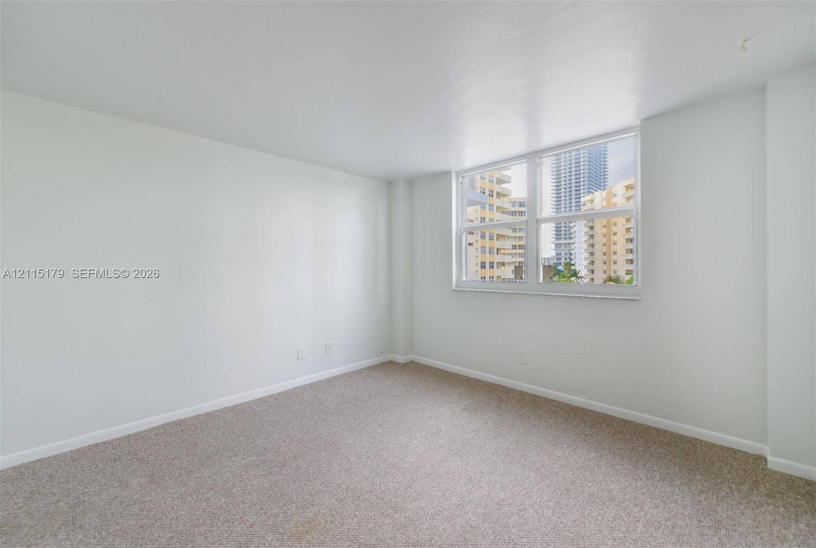 1849 S Ocean Drive, #407, Hallandale Beach, Hallandale Beach, FL 33009 Interior space featuring neutral wall tones, wall-to-wall carpeting, and a large multi-pane window with urban exterior surroundings