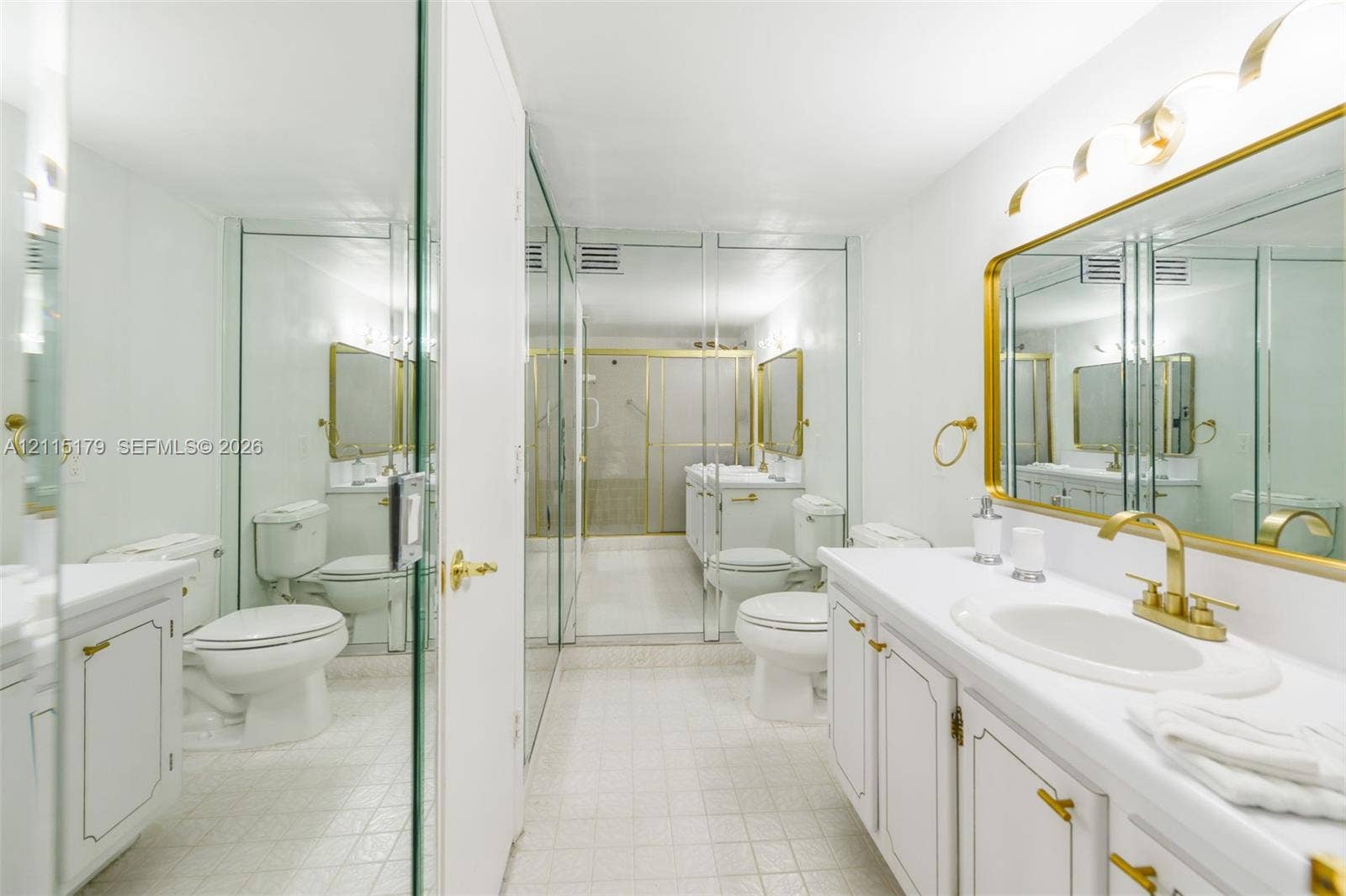 1849 S Ocean Drive, #407, Hallandale Beach, Hallandale Beach, FL 33009 Bathroom featuring a white vanity with gold-tone hardware, an oval undermount sink, a framed gold-tone mirror, mirrored wall panels, and tiled flooring