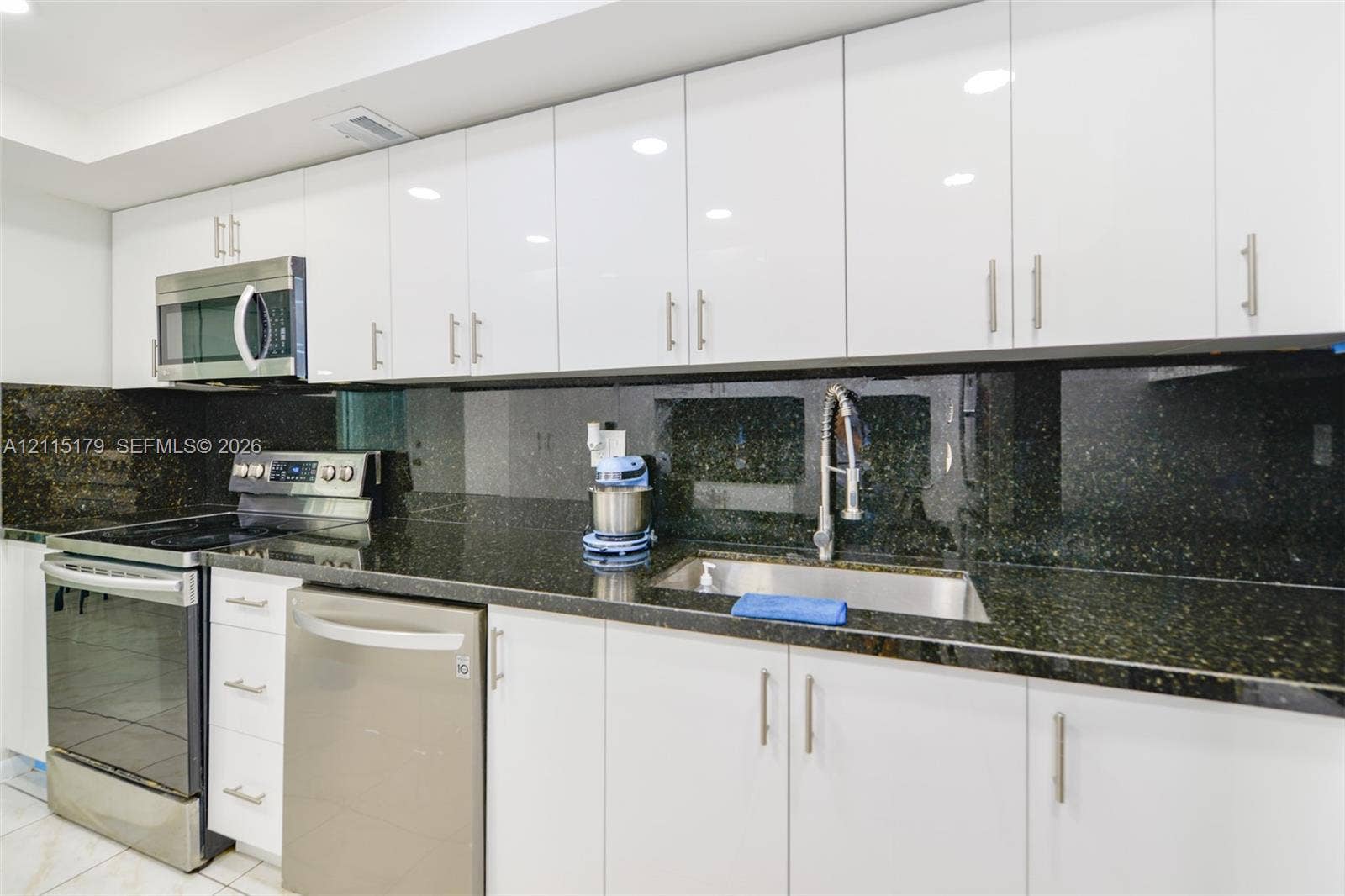 1849 S Ocean Drive, #407, Hallandale Beach, Hallandale Beach, FL 33009 Kitchen featuring high-gloss white cabinetry, dark stone countertops, full-height stone backsplash, stainless steel appliances, and a pull-down faucet