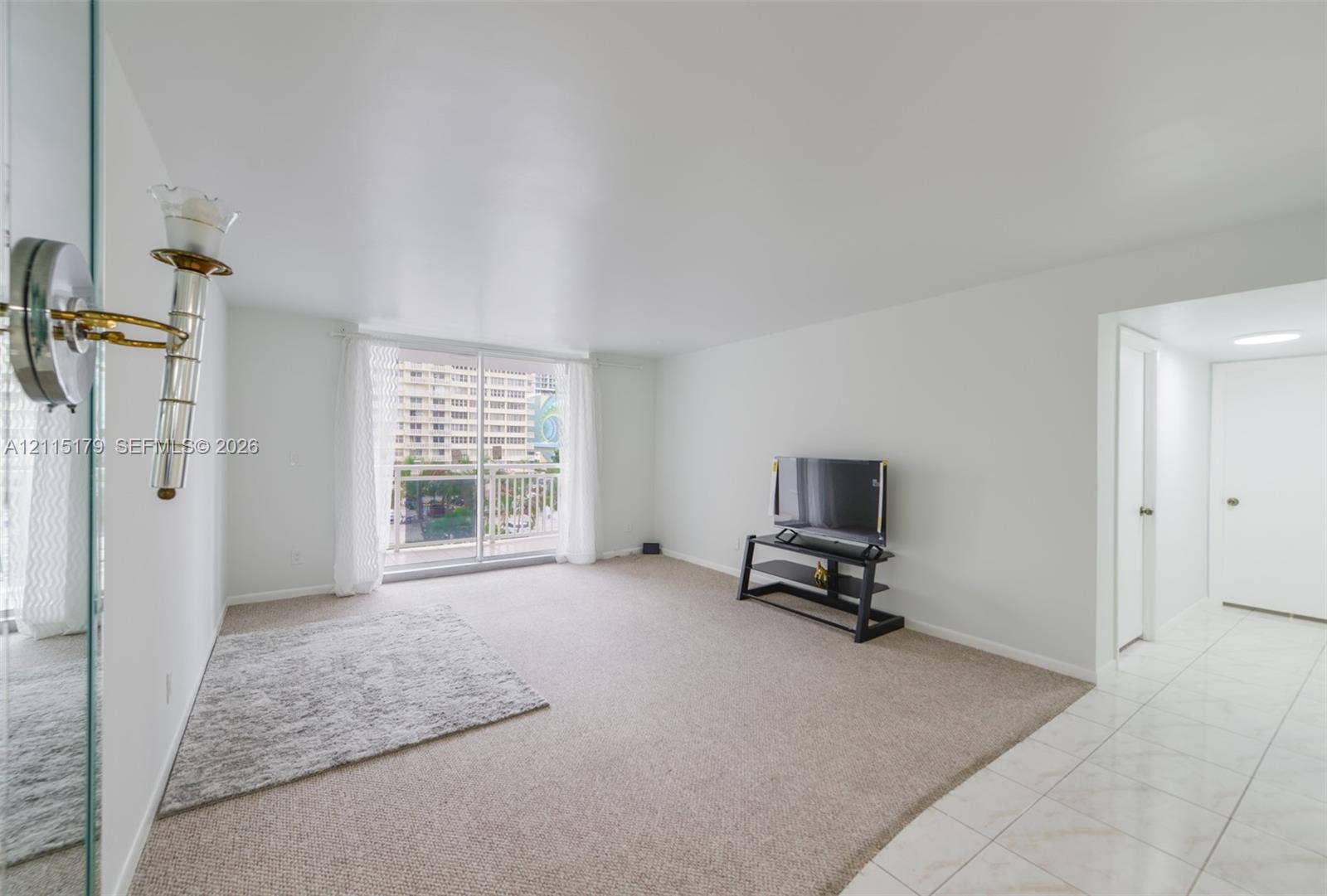1849 S Ocean Drive, #407, Hallandale Beach, Hallandale Beach, FL 33009 Living area featuring neutral carpeting, ceramic tile flooring, sliding glass door to a balcony, and wall-mounted brass and glass light fixture