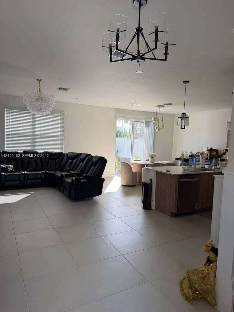 721 SE 17th Avenue, #721, Homestead, Homestead, FL 33033 Open floor plan featuring large-format tile flooring, a kitchen island with stone countertops, sliding glass patio doors, and multi-light chandelier fixtures