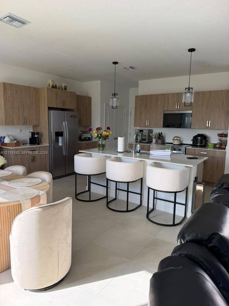 721 SE 17th Avenue, #721, Homestead, Homestead, FL 33033 Kitchen featuring wood-finish cabinetry, a stone-surface island, stainless steel appliances, and dual pendant light fixtures