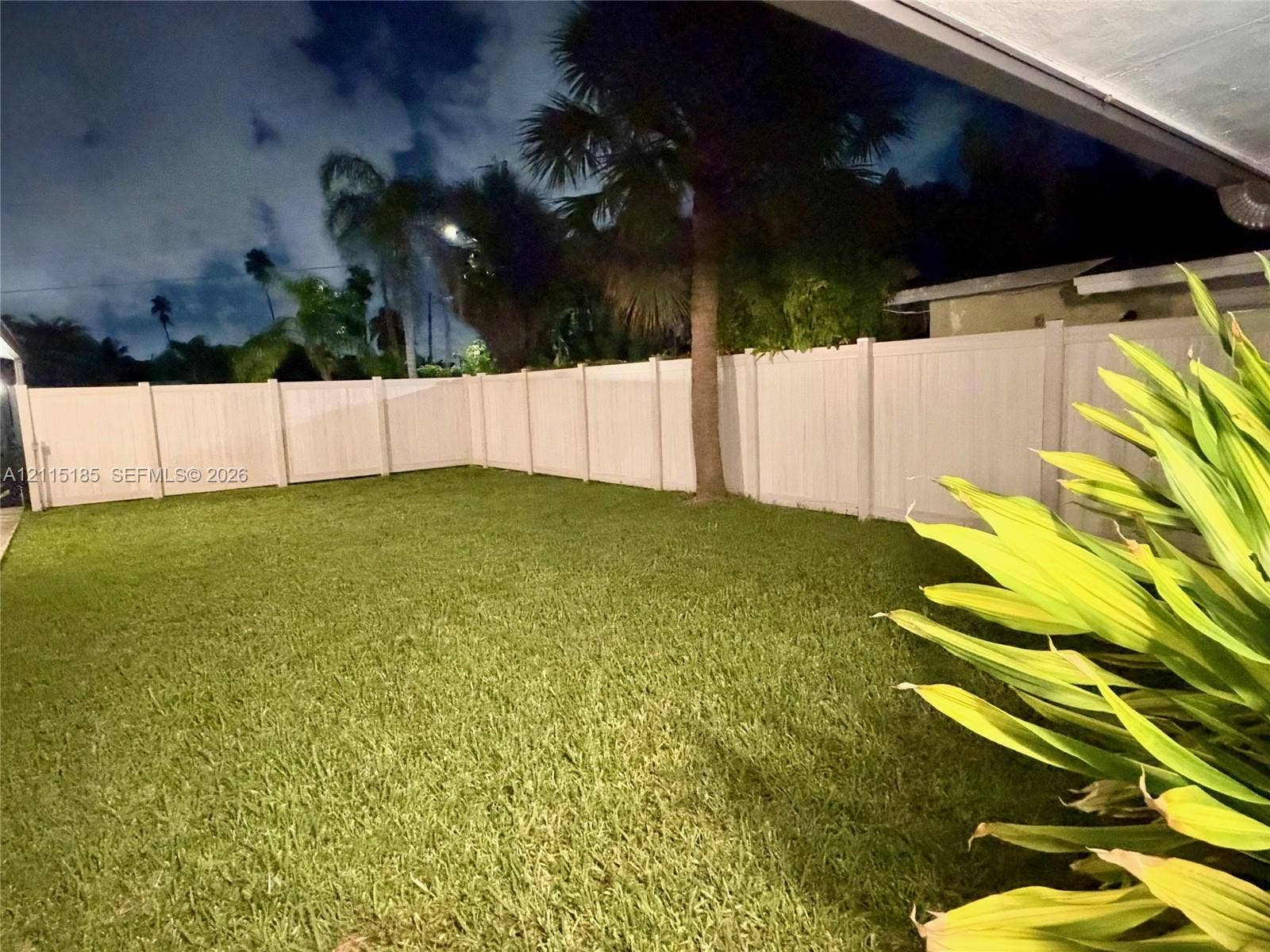 105-107 NE 30th Court, Wilton Manors, FL 33334 Backyard featuring a manicured lawn, full-perimeter white vinyl fencing, and mature palm trees