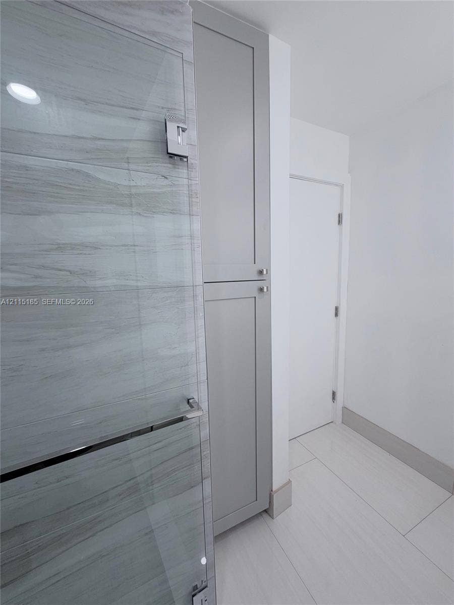 105-107 NE 30th Court, Wilton Manors, FL 33334 Floor-to-ceiling cabinetry with gray shaker-style doors, glass-enclosed shower featuring horizontal stone-patterned tile, and large-format porcelain tile flooring