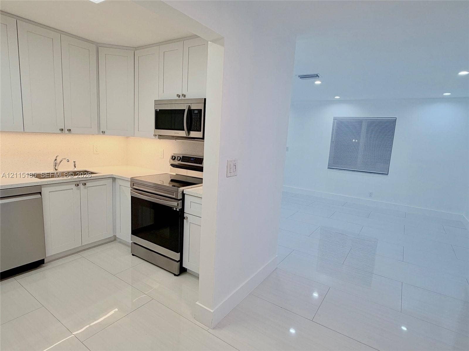105-107 NE 30th Court, Wilton Manors, FL 33334 Kitchen featuring white shaker-style cabinetry, solid-surface countertops, and stainless steel appliances, complemented by large-format tile flooring and recessed lighting