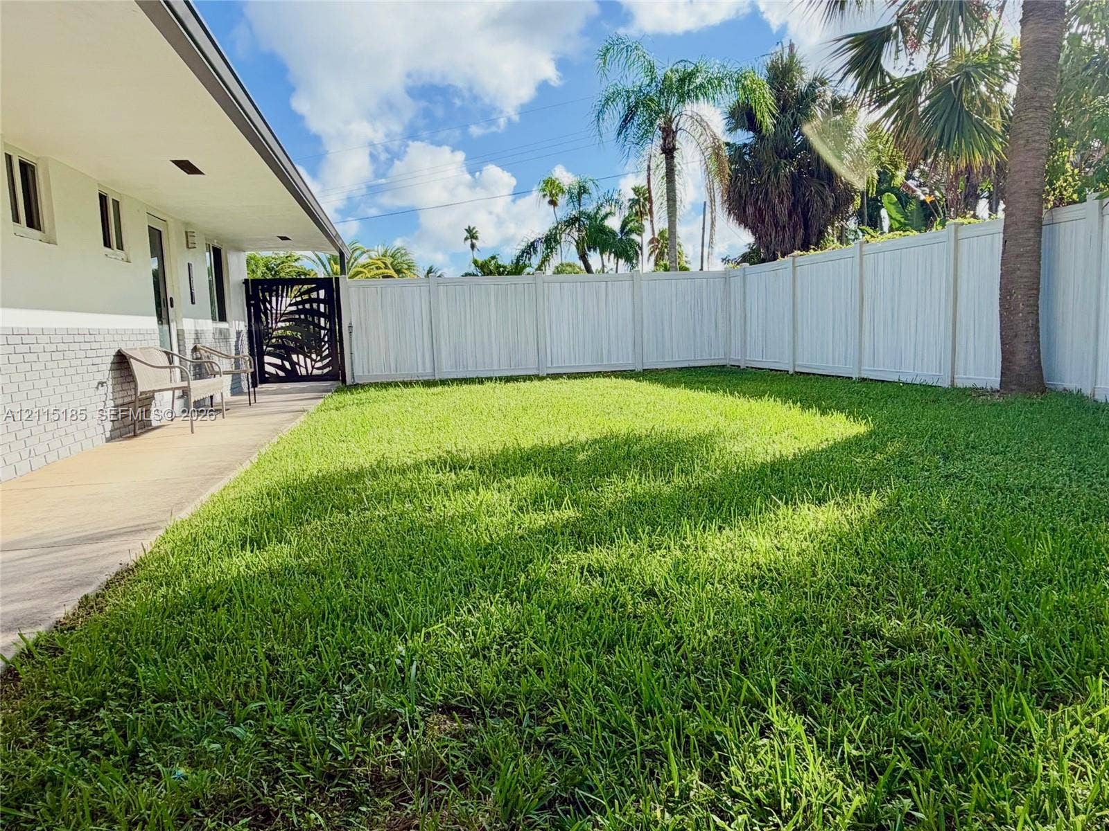 105-107 NE 30th Court, Wilton Manors, FL 33334 Backyard featuring a paved covered patio, manicured lawn, white vinyl fencing, and an ornate metal gate
