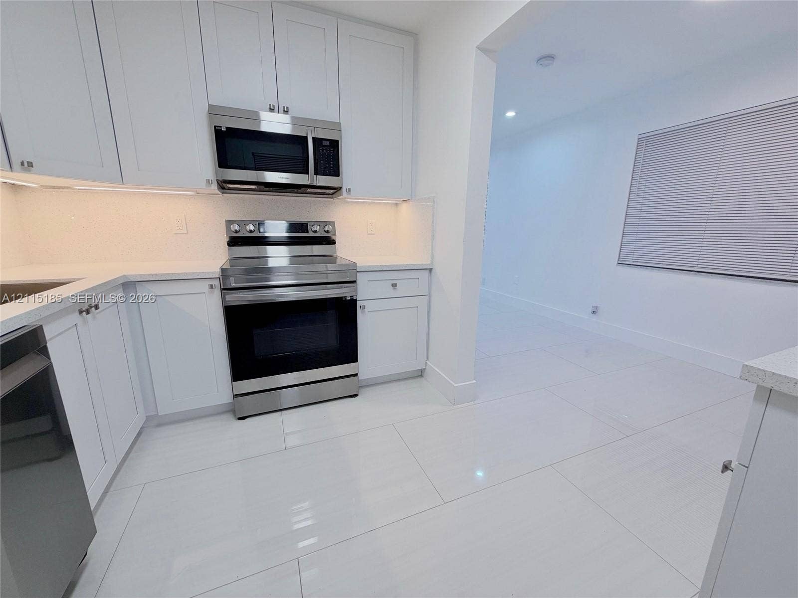 105-107 NE 30th Court, Wilton Manors, FL 33334 Kitchen featuring white shaker-style cabinetry, stainless steel appliances, under-cabinet lighting, solid surface countertops, and large-format porcelain tile flooring