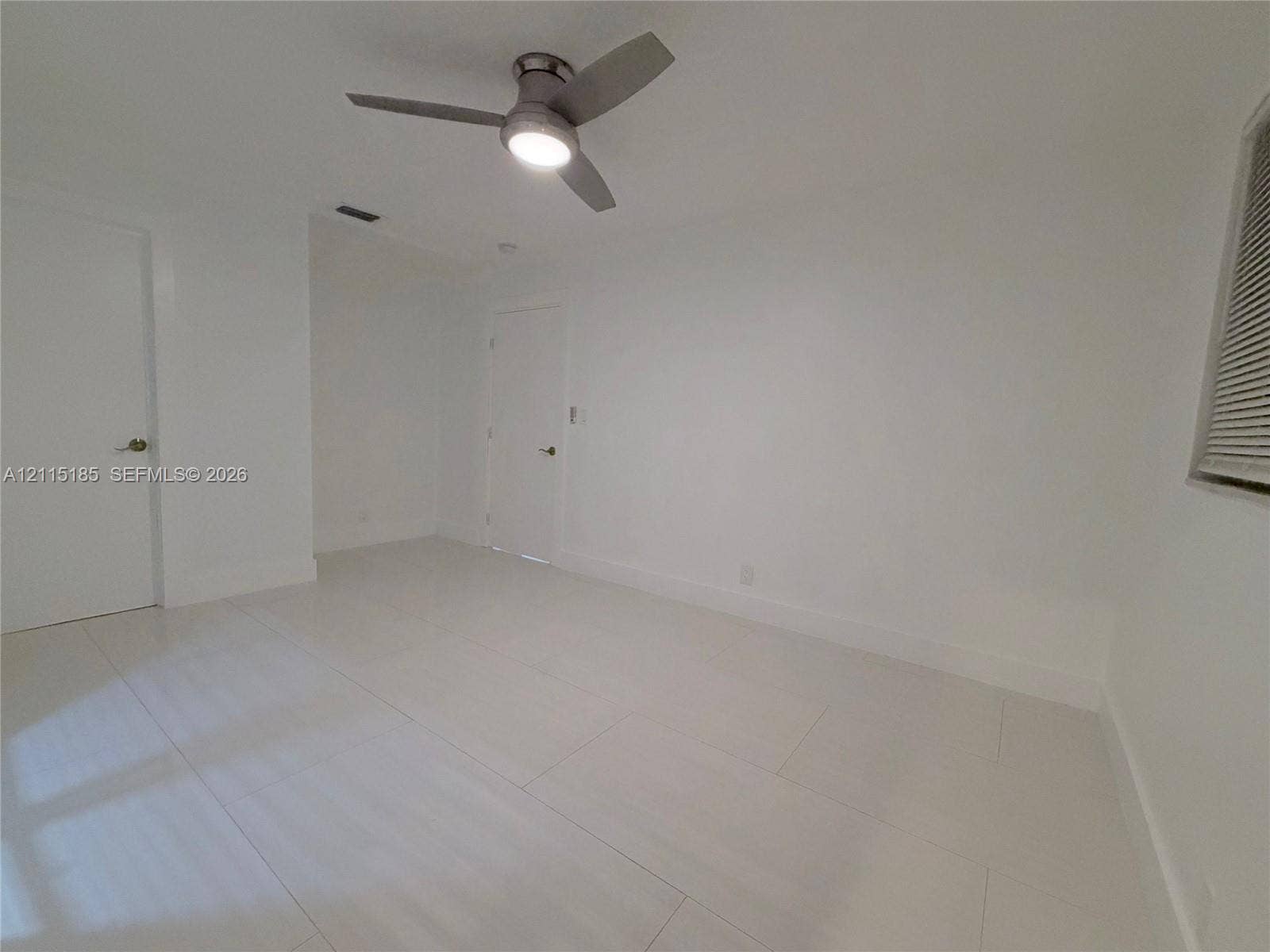 105-107 NE 30th Court, Wilton Manors, FL 33334 Neutral-toned interior featuring large-format tile flooring, a modern three-blade ceiling fan with integrated lighting, and white interior doors with satin nickel hardware