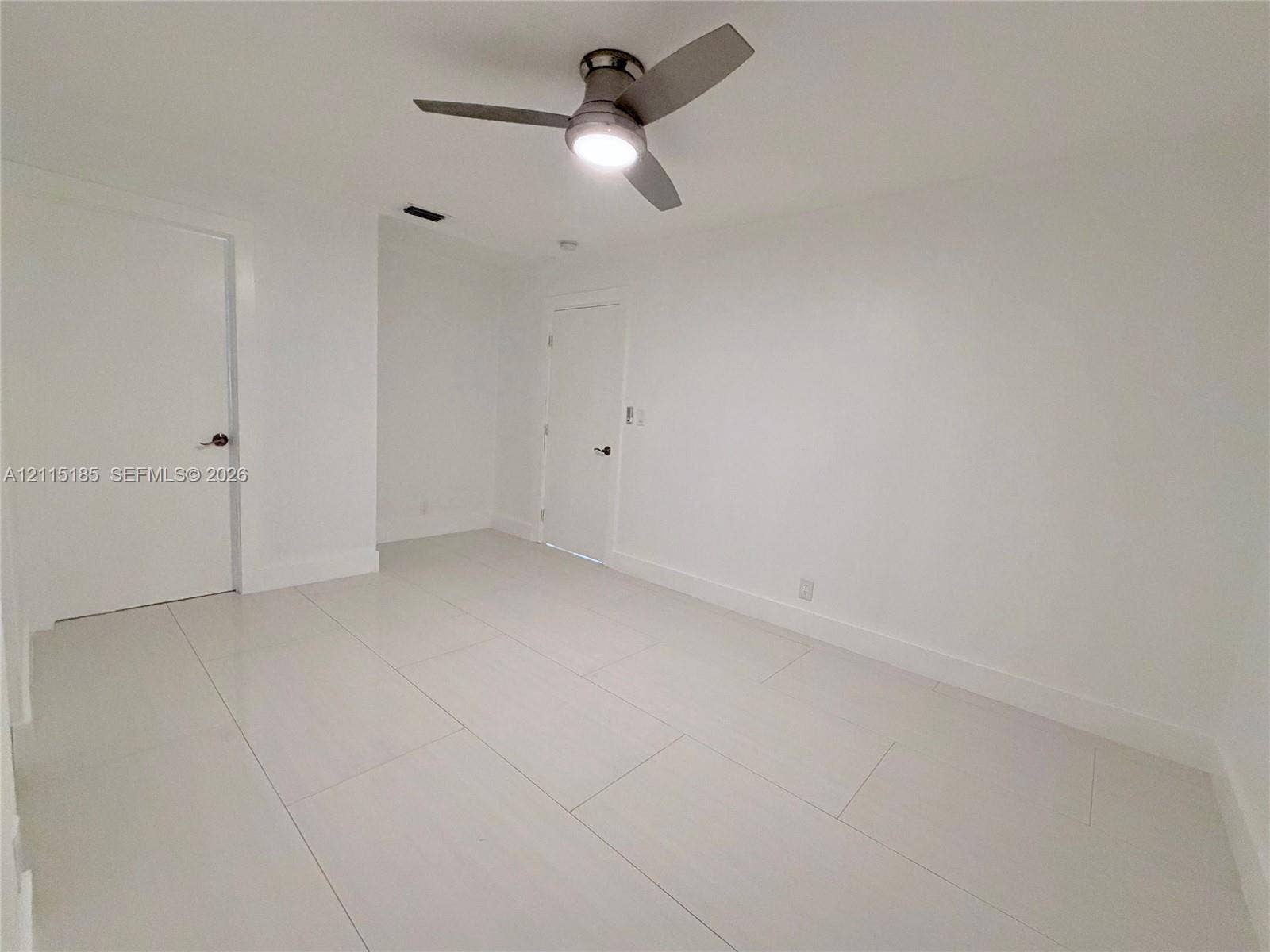 105-107 NE 30th Court, Wilton Manors, FL 33334 Interior space featuring large-format porcelain tile flooring, smooth wall finishes, two interior doors with matte-finish hardware, and a modern three-blade ceiling fan with integrated lighting