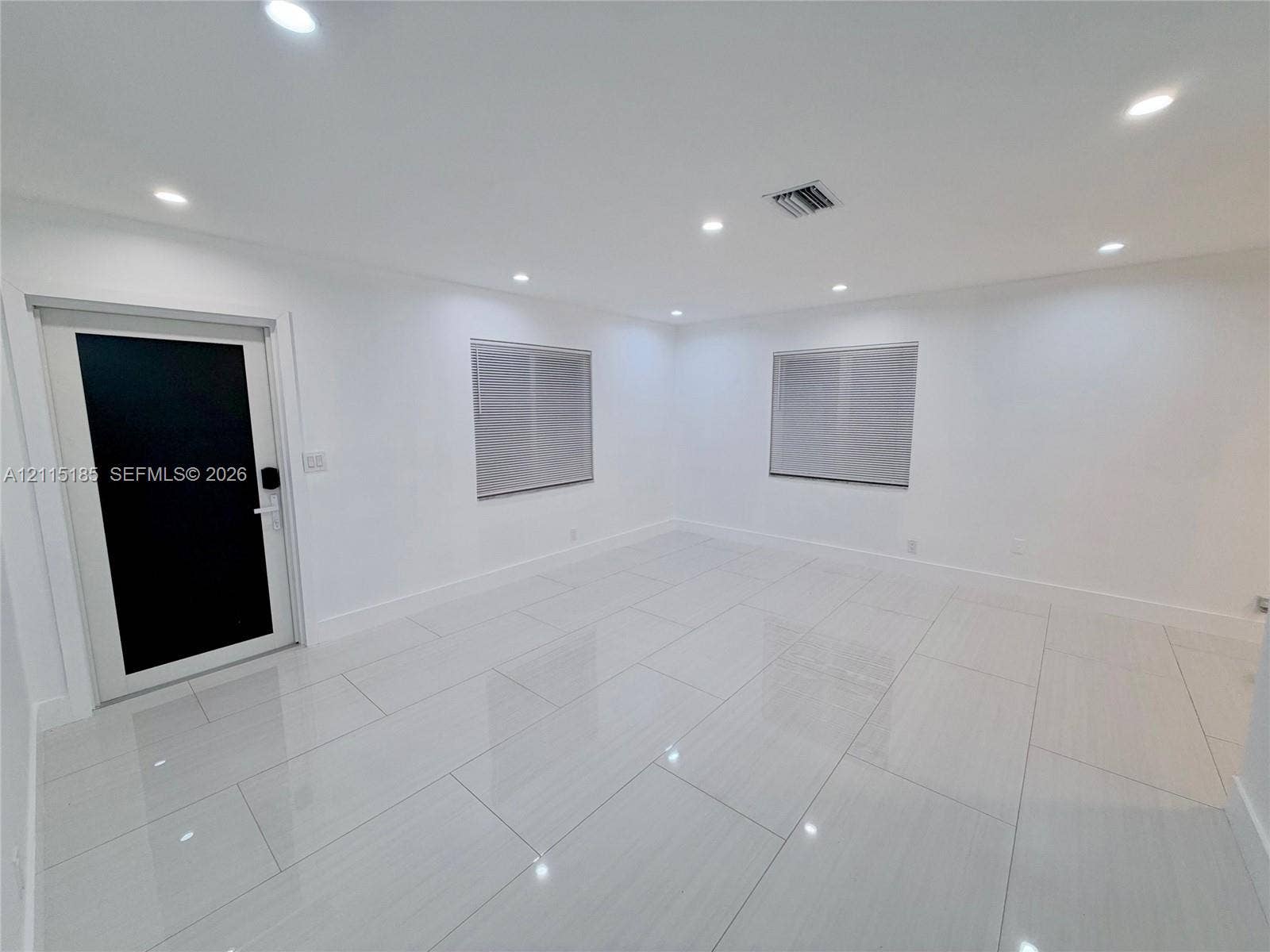 105-107 NE 30th Court, Wilton Manors, FL 33334 Interior space featuring high-gloss tile flooring, recessed ceiling lighting, and a modern black-paneled entry door with hardware