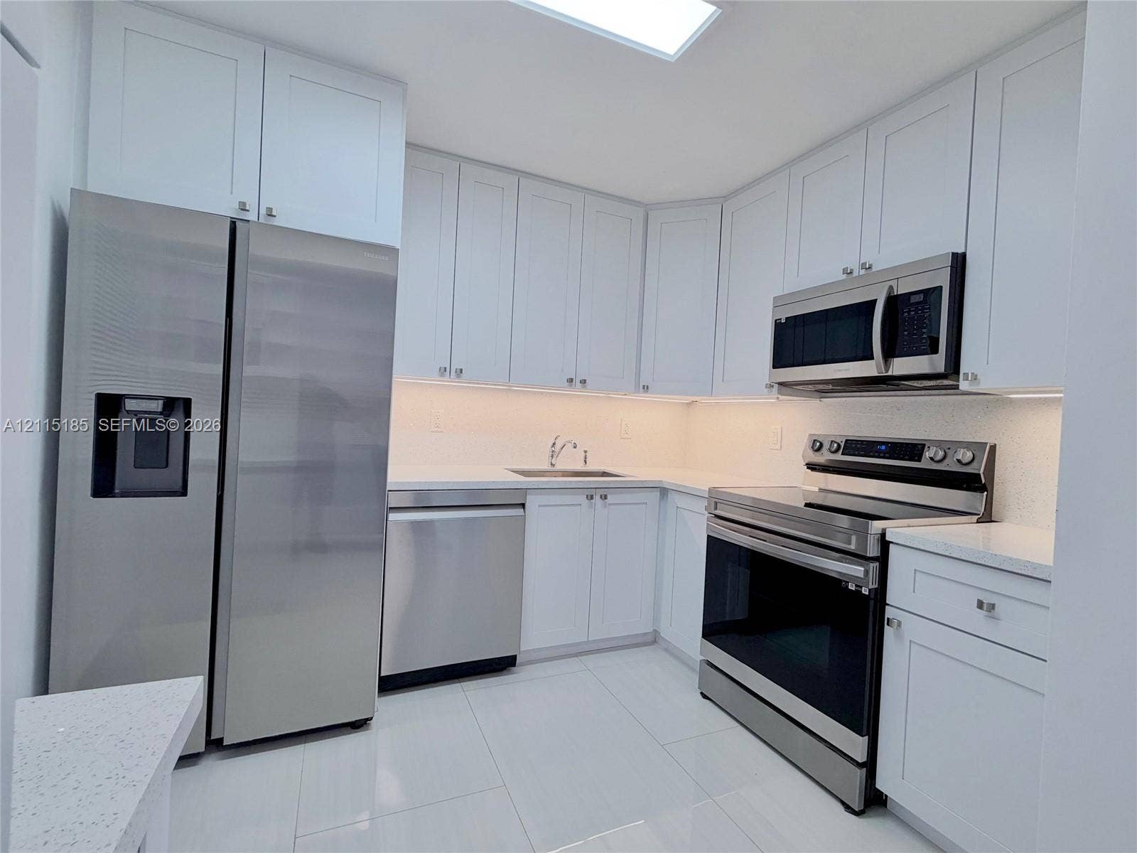 105-107 NE 30th Court, Wilton Manors, FL 33334 Kitchen featuring white shaker-style cabinetry, quartz countertops, stainless steel appliances, large-format tile flooring, and a recessed skylight
