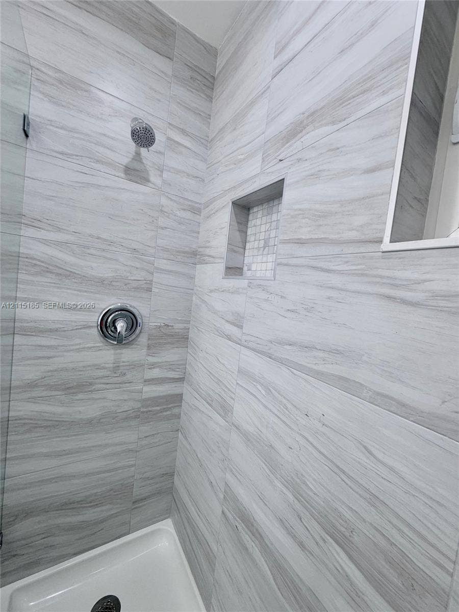 105-107 NE 30th Court, Wilton Manors, FL 33334 Shower enclosure featuring large-format neutral-toned tile, built-in recessed niche with mosaic accent, glass panel, and polished chrome shower fixtures