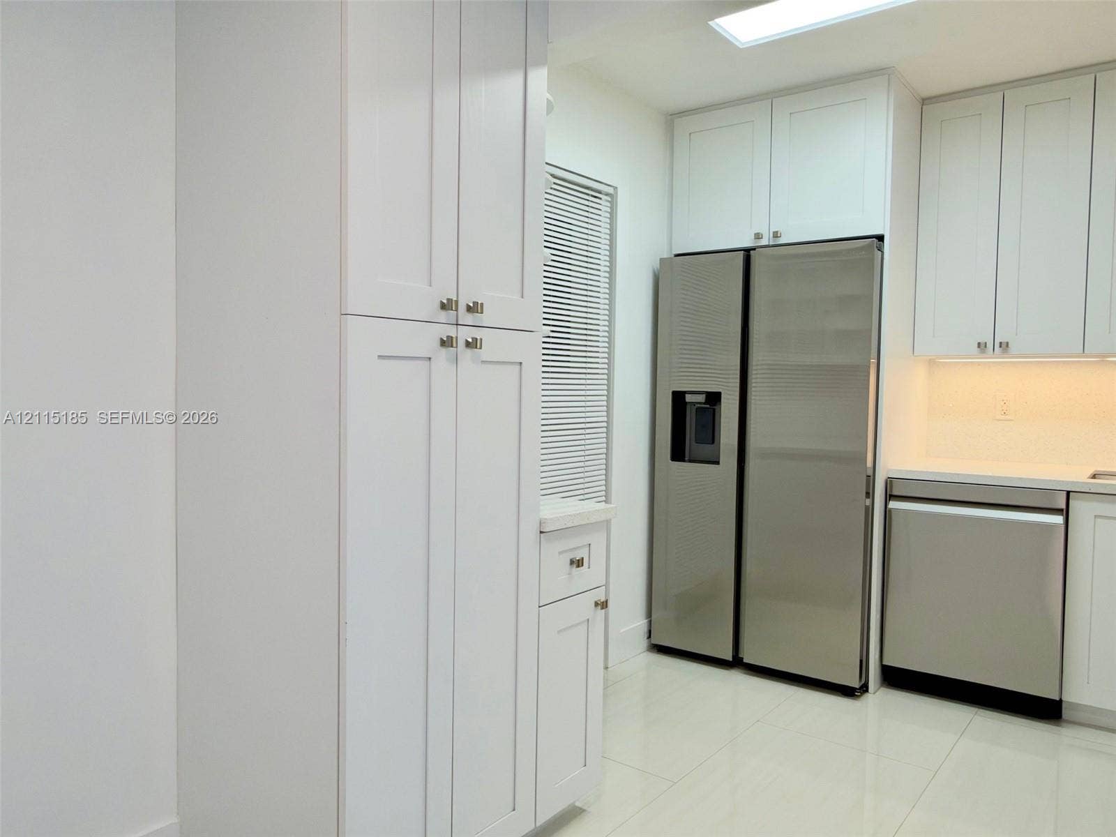 105-107 NE 30th Court, Wilton Manors, FL 33334 Kitchen featuring white shaker-style cabinetry, stainless steel appliances, polished stone-finish countertops, tile flooring, and a ceiling skylight