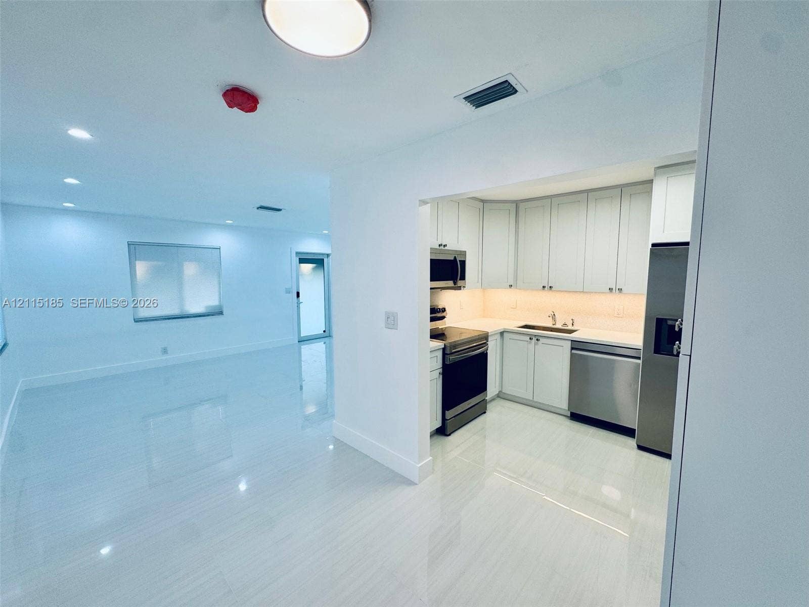 105-107 NE 30th Court, Wilton Manors, FL 33334 Kitchen featuring white shaker-style cabinetry, solid-surface countertops, stainless steel appliances, and tile flooring throughout