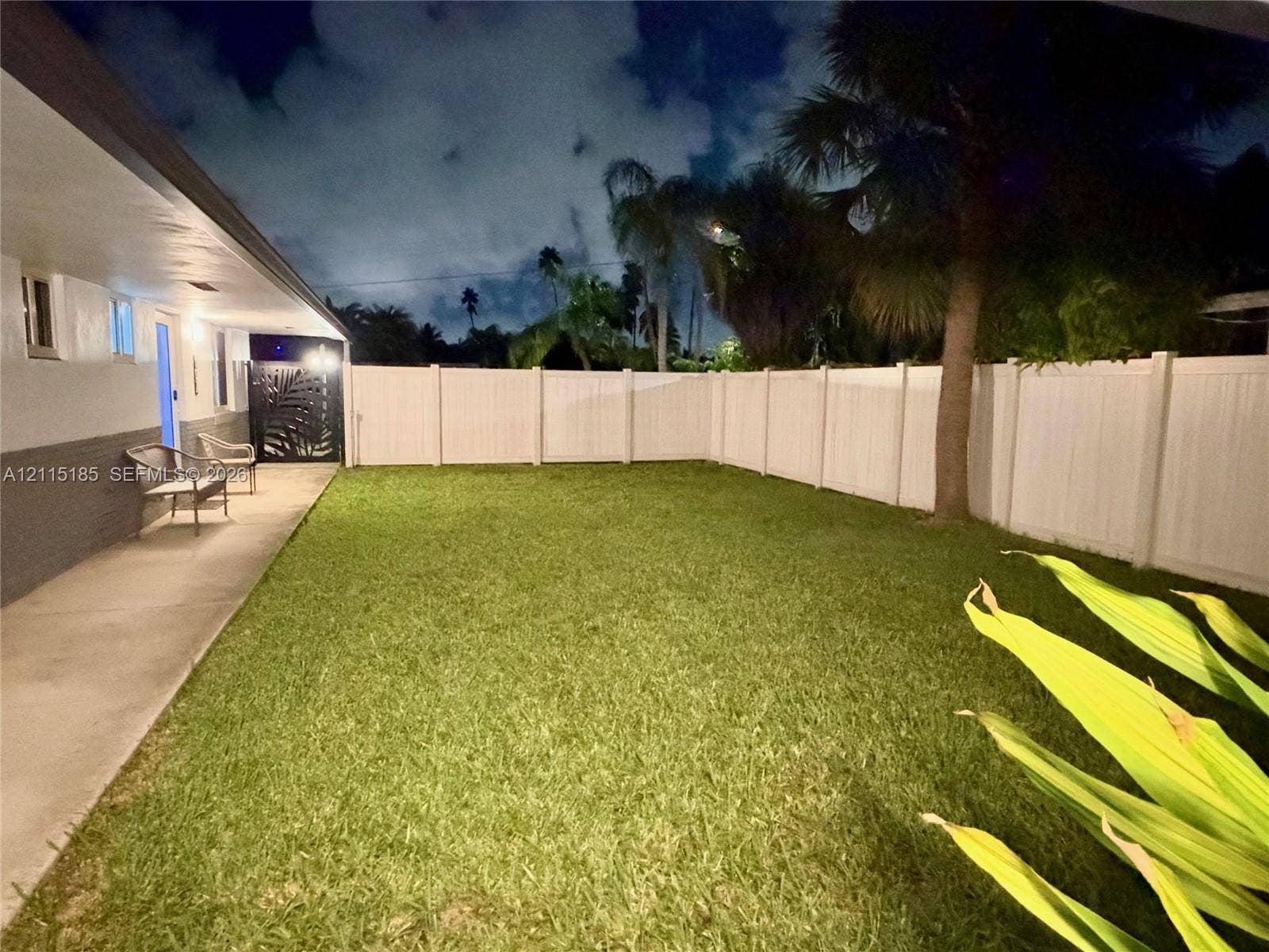 105-107 NE 30th Court, Wilton Manors, FL 33334 Private backyard featuring a concrete patio, white vinyl fencing, manicured lawn, and mature palm trees
