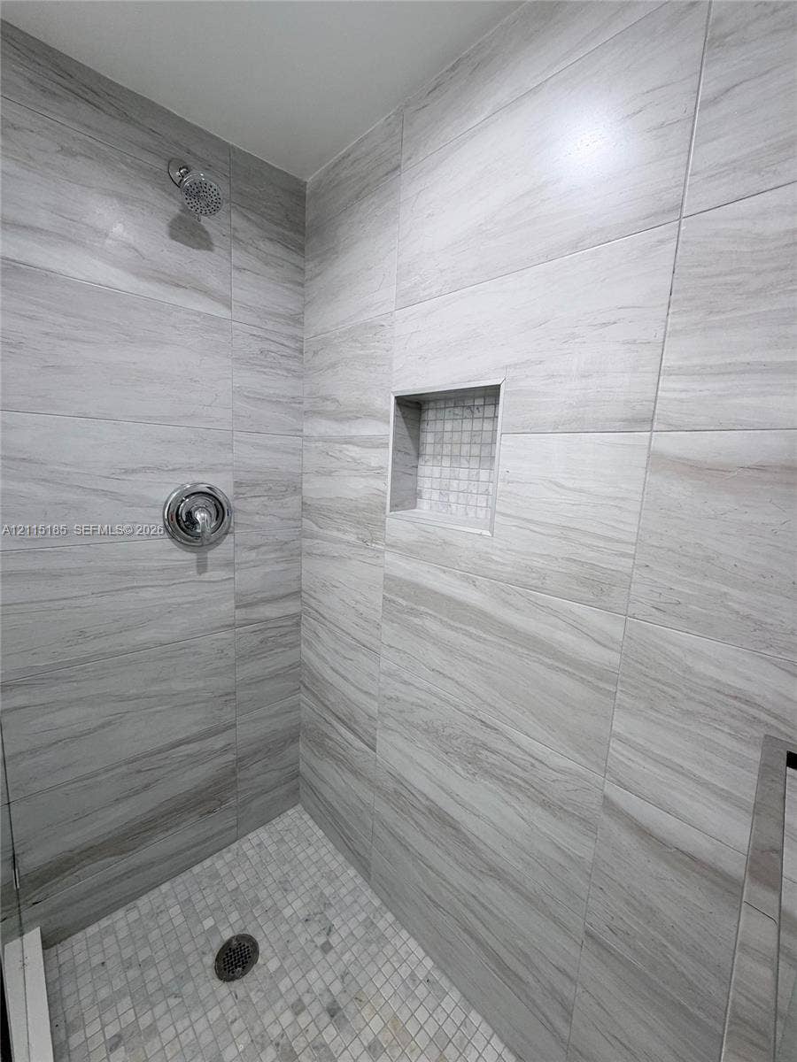 105-107 NE 30th Court, Wilton Manors, FL 33334 Walk-in shower featuring large-format neutral-toned wall tile, a recessed tiled niche, a mosaic-tiled floor, and a circular shower head with a round control handle