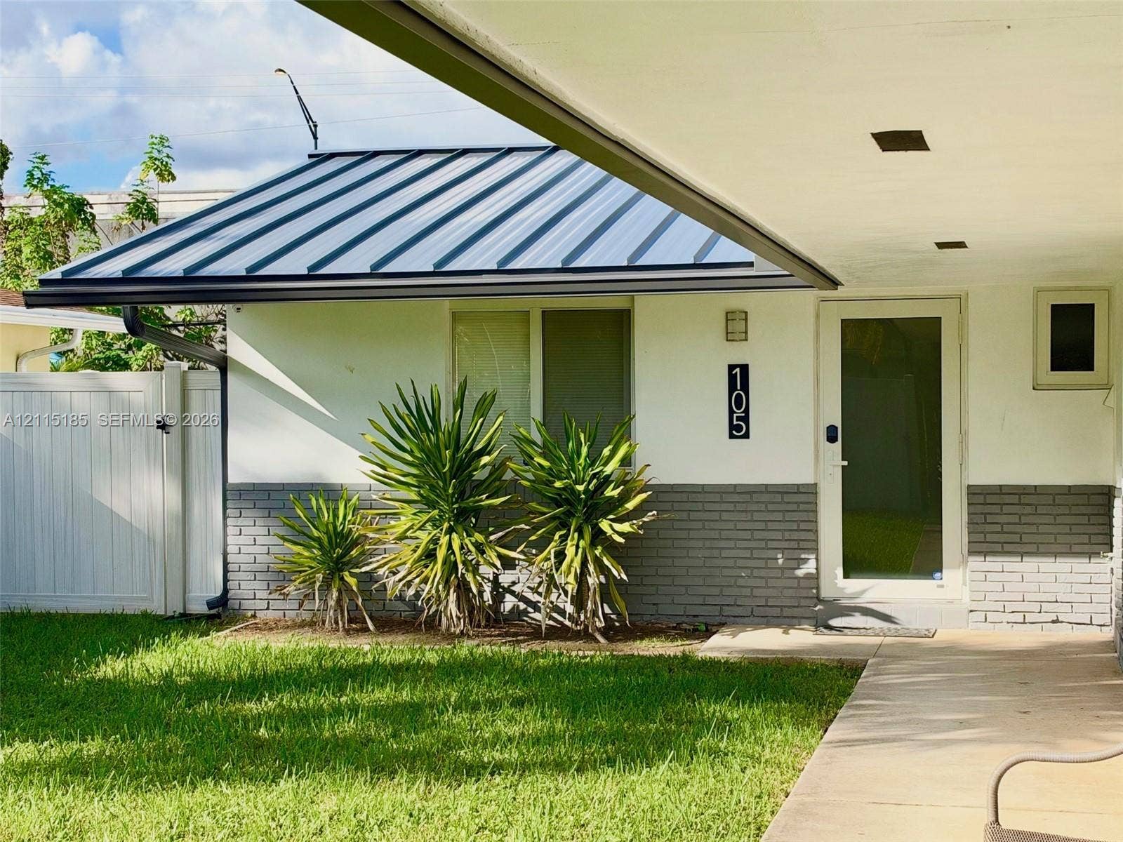 105-107 NE 30th Court, Wilton Manors, FL 33334 Exterior featuring a standing-seam metal roof, white stucco walls with gray brick veneer, a covered entryway, and a white privacy fence