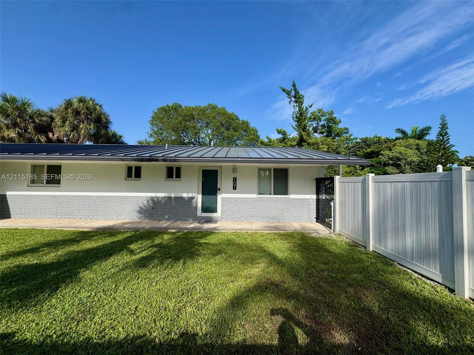 105-107 NE 30th Court, Wilton Manors, FL 33334 Exterior featuring a metal roof, two-tone masonry and stucco siding, a paved walkway, and a full-height vinyl privacy fence