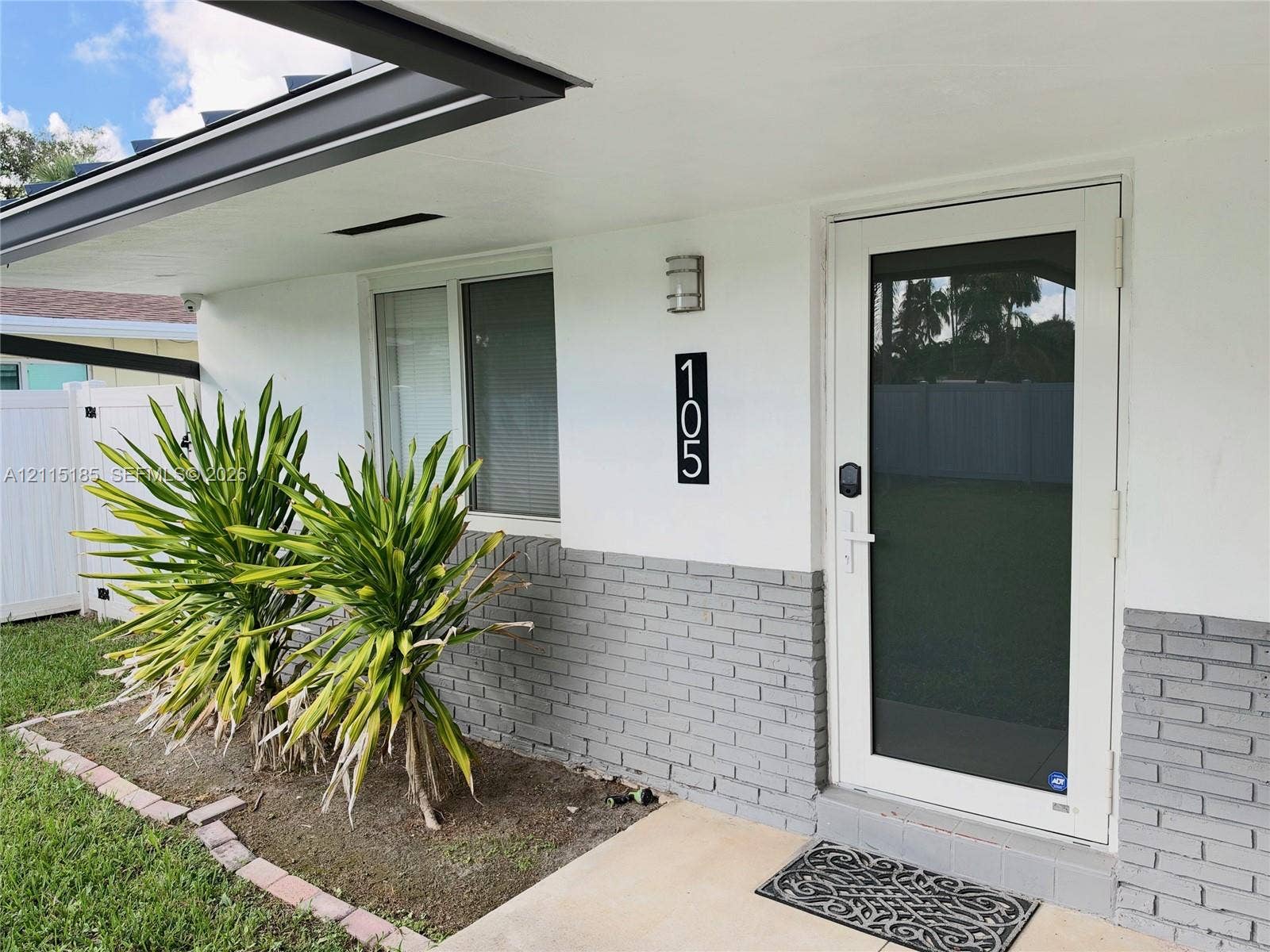 105-107 NE 30th Court, Wilton Manors, FL 33334 Exterior entrance featuring a white-painted finish with a gray brick wainscot, a full-view storm door, a covered porch, and a brick-edged landscape bed