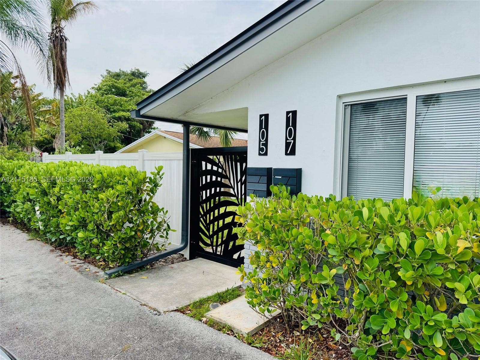 105-107 NE 30th Court, Wilton Manors, FL 33334 Stucco exterior with a metal decorative gate, privacy fencing, and professional landscaping