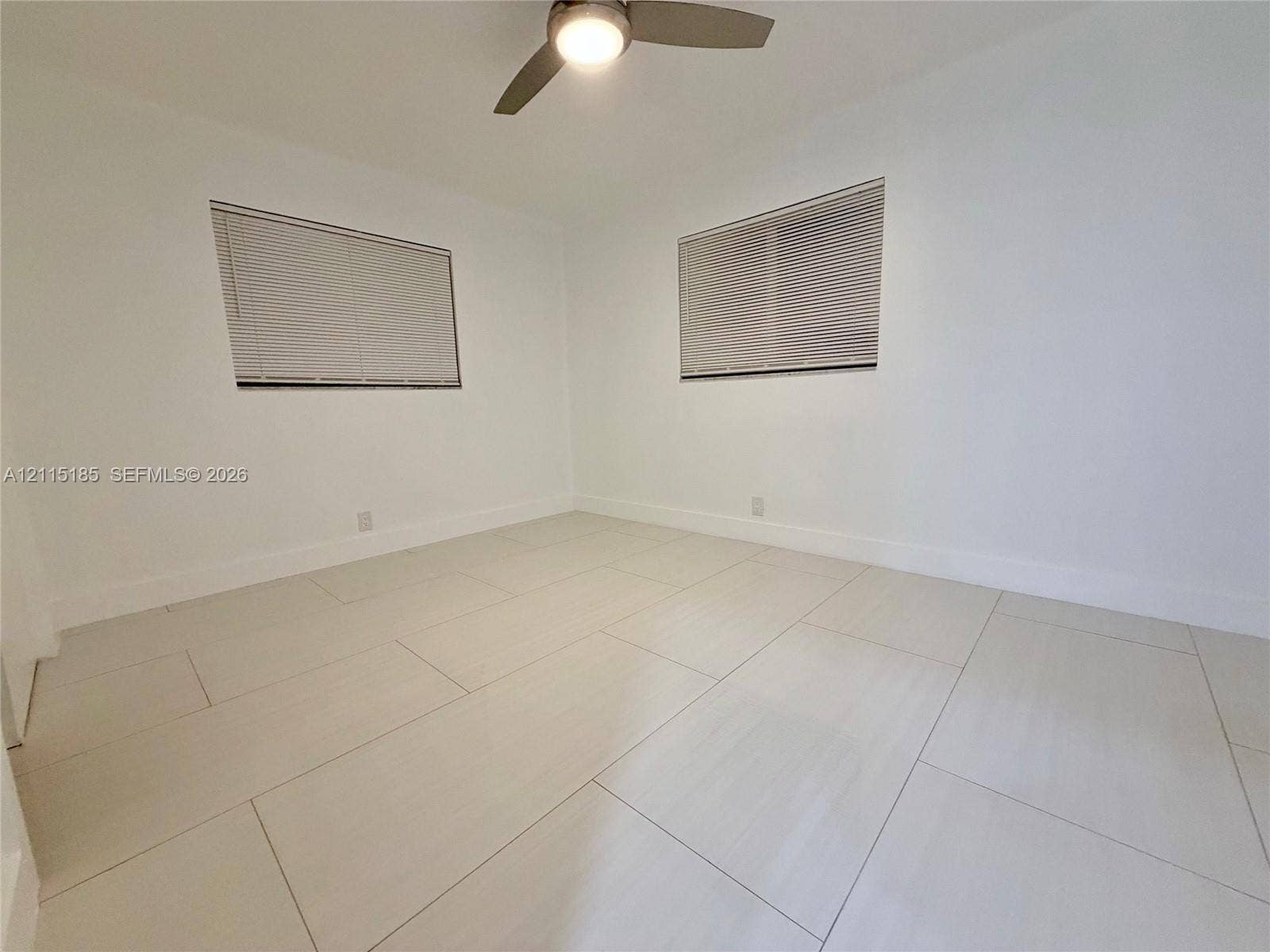 105-107 NE 30th Court, Wilton Manors, FL 33334 Bright interior featuring large-format tile flooring, neutral walls, two windows with horizontal blinds, and a central ceiling fan with integrated lighting