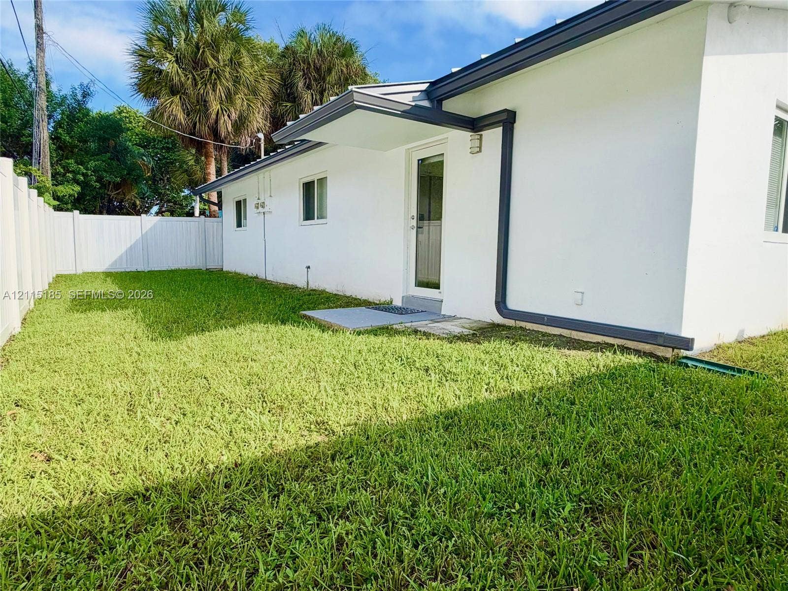 105-107 NE 30th Court, Wilton Manors, FL 33334 Exterior side yard featuring a manicured lawn, full-height privacy fencing, and a covered entryway with an exterior glass-panel door