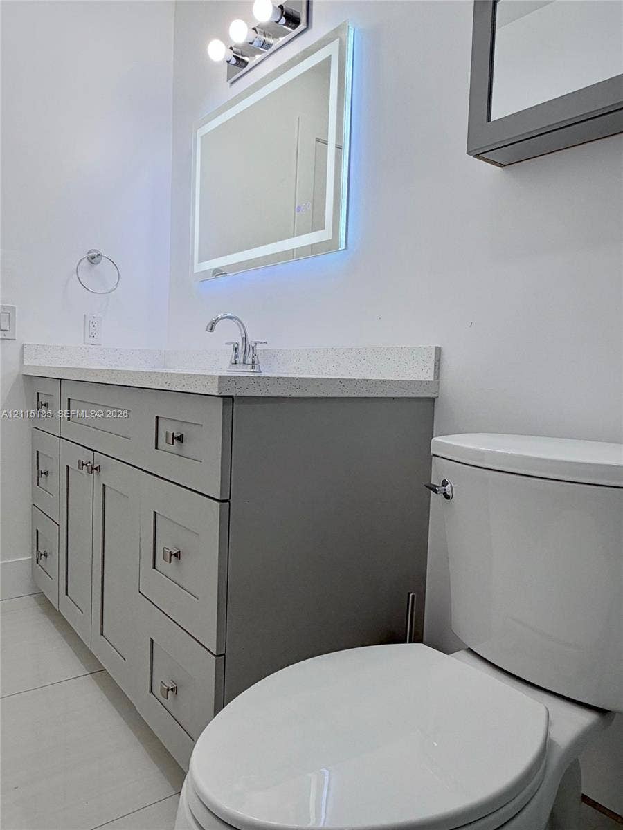 105-107 NE 30th Court, Wilton Manors, FL 33334 Gray shaker-style vanity with stone-composite countertop, illuminated LED vanity mirror, chrome faucet, and tiled flooring