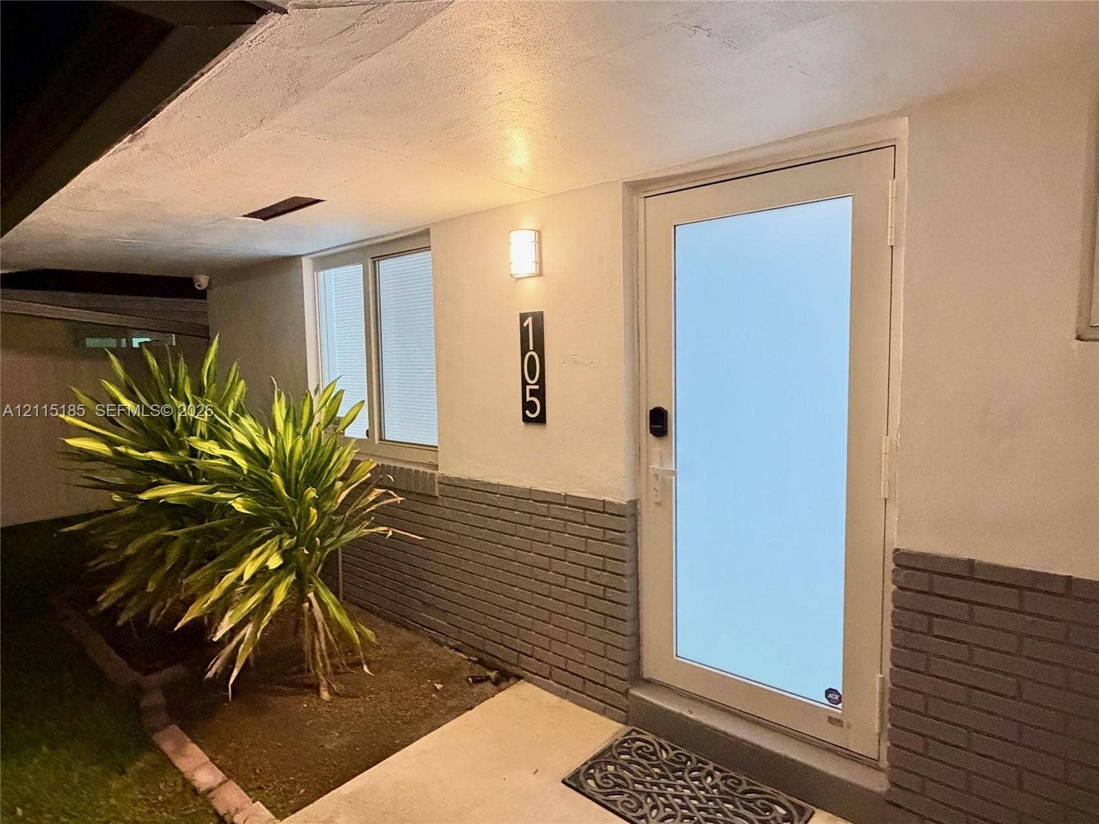 105-107 NE 30th Court, Wilton Manors, FL 33334 Exterior entry featuring a glass-panel door, lower brick masonry siding, a wall-mounted light fixture, and vertical address signage
