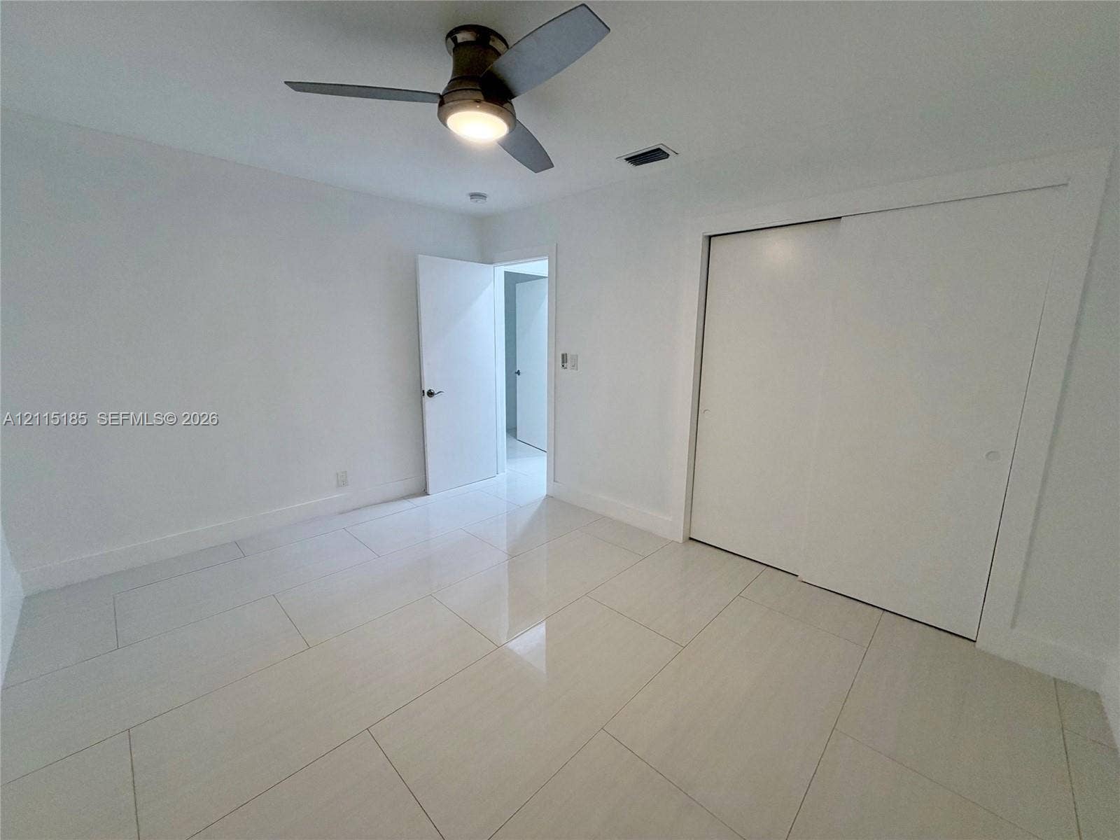 105-107 NE 30th Court, Wilton Manors, FL 33334 Neutral-toned interior space featuring polished large-format tile flooring, a dual-panel sliding closet, and a ceiling-mounted light fixture with an integrated fan