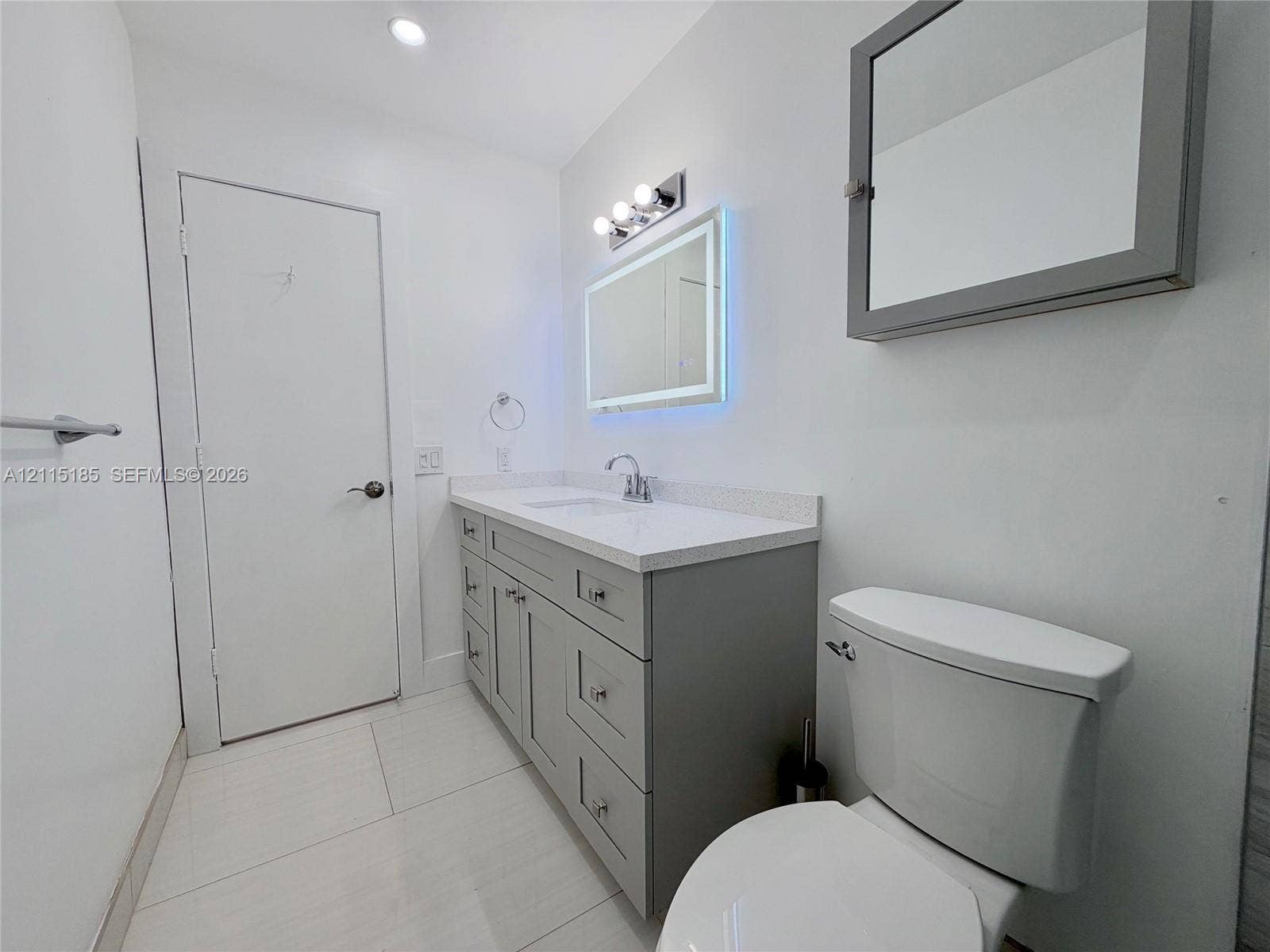 105-107 NE 30th Court, Wilton Manors, FL 33334 Bathroom featuring a gray vanity with a stone countertop, an integrated sink, an illuminated vanity mirror, and large-format tile flooring