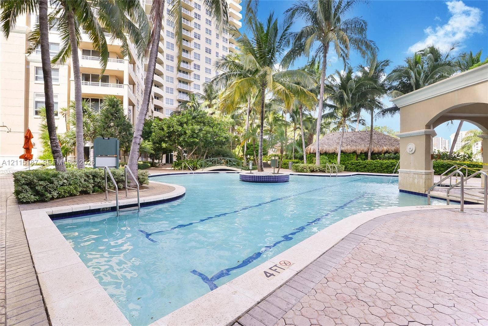 19501 W Country Club Drive, #504, Aventura, Aventura, FL 33180 Swimming pool with a paved deck, surrounding palm trees, thatched-roof structure, and arched architectural detailing