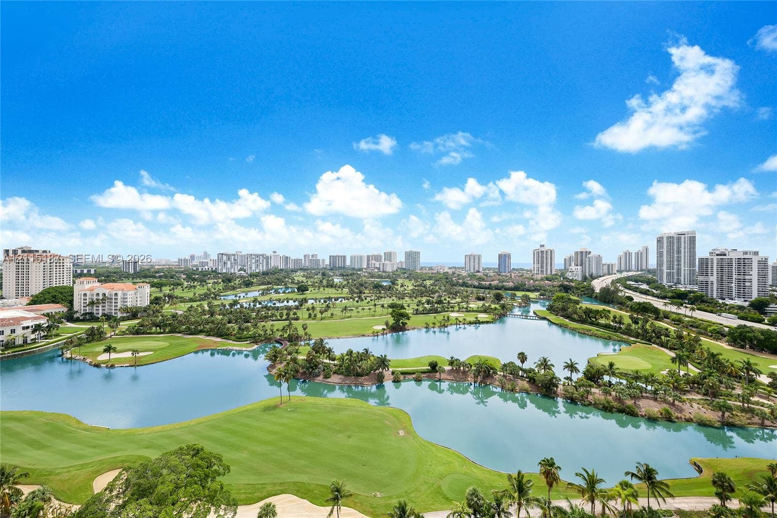 19501 W Country Club Drive, #504, Aventura, Aventura, FL 33180 Panoramic perspective featuring a golf course, expansive water features, mature palm trees, and an urban skyline