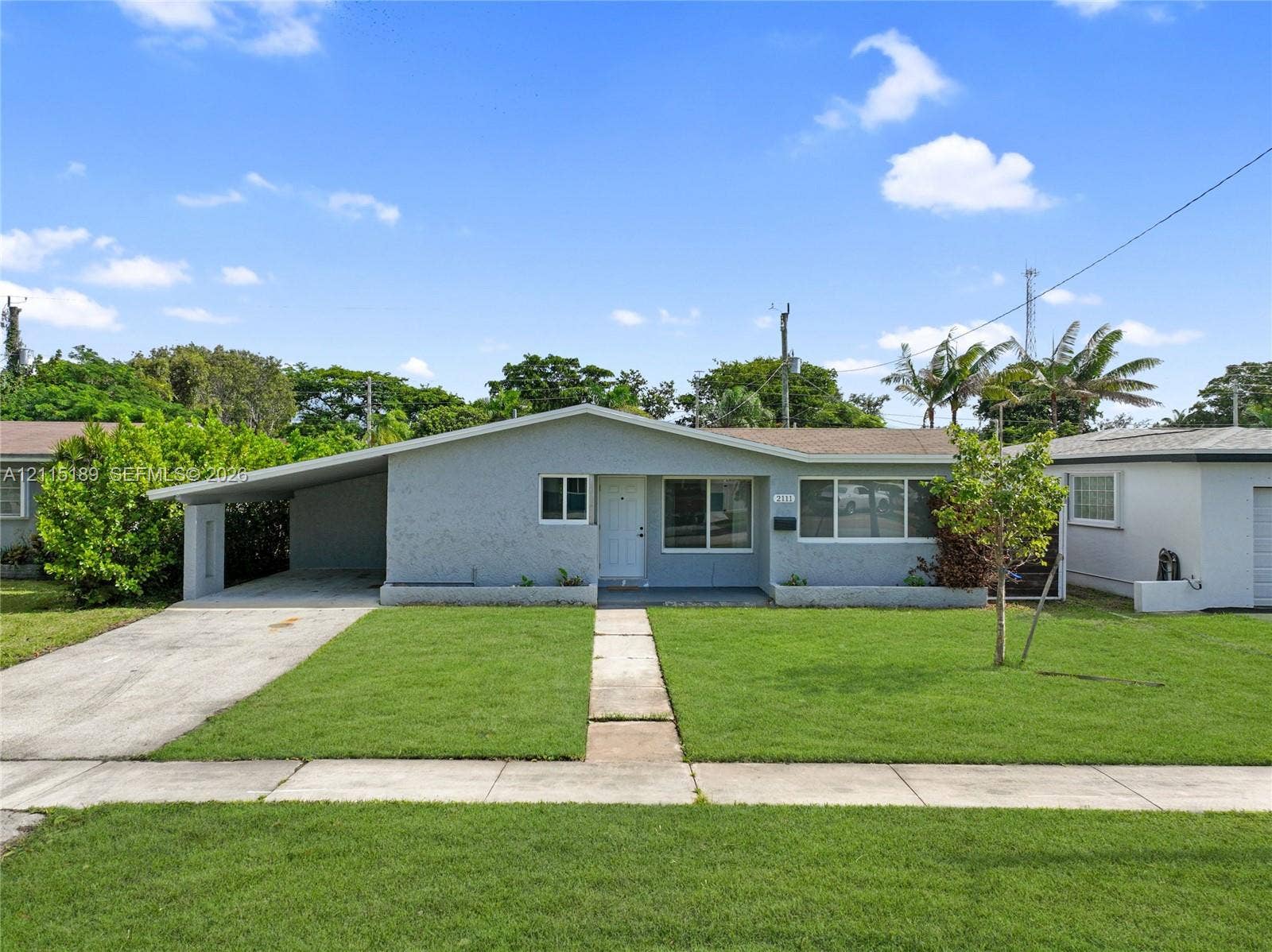 2111 N 14th Court, Hollywood, Hollywood, FL 33020 Single-story exterior featuring a light gray stucco finish, an attached carport, a concrete driveway, and a front lawn with established landscaping