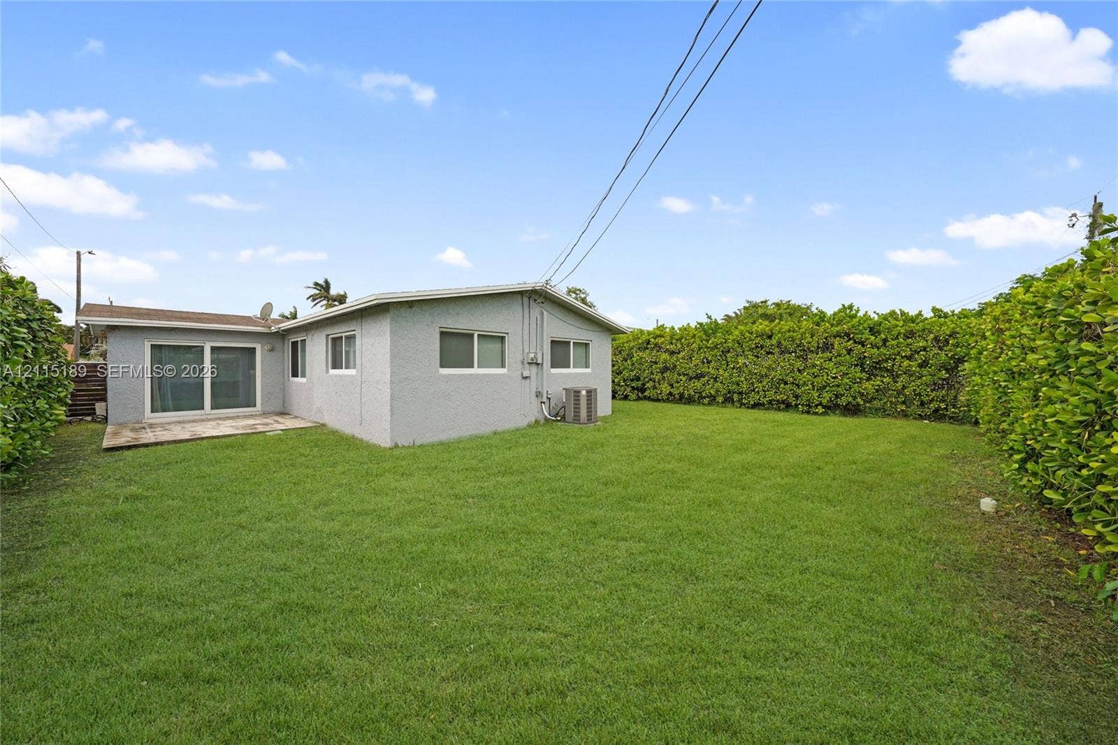 2111 N 14th Court, Hollywood, Hollywood, FL 33020 Spacious backyard featuring a grass lawn, concrete patio, sliding glass door, and mature privacy hedging