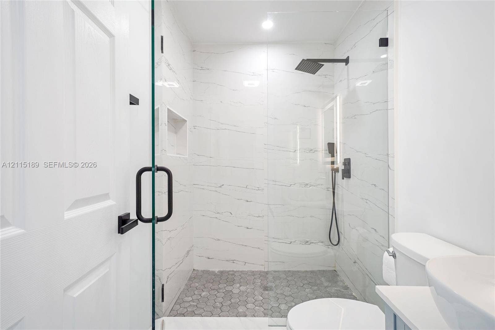 2111 N 14th Court, Hollywood, Hollywood, FL 33020 Walk-in shower featuring large-format wall tile, a frameless glass enclosure, a built-in recessed niche, a rainfall showerhead with matte black finish, and a hexagonal tile shower floor