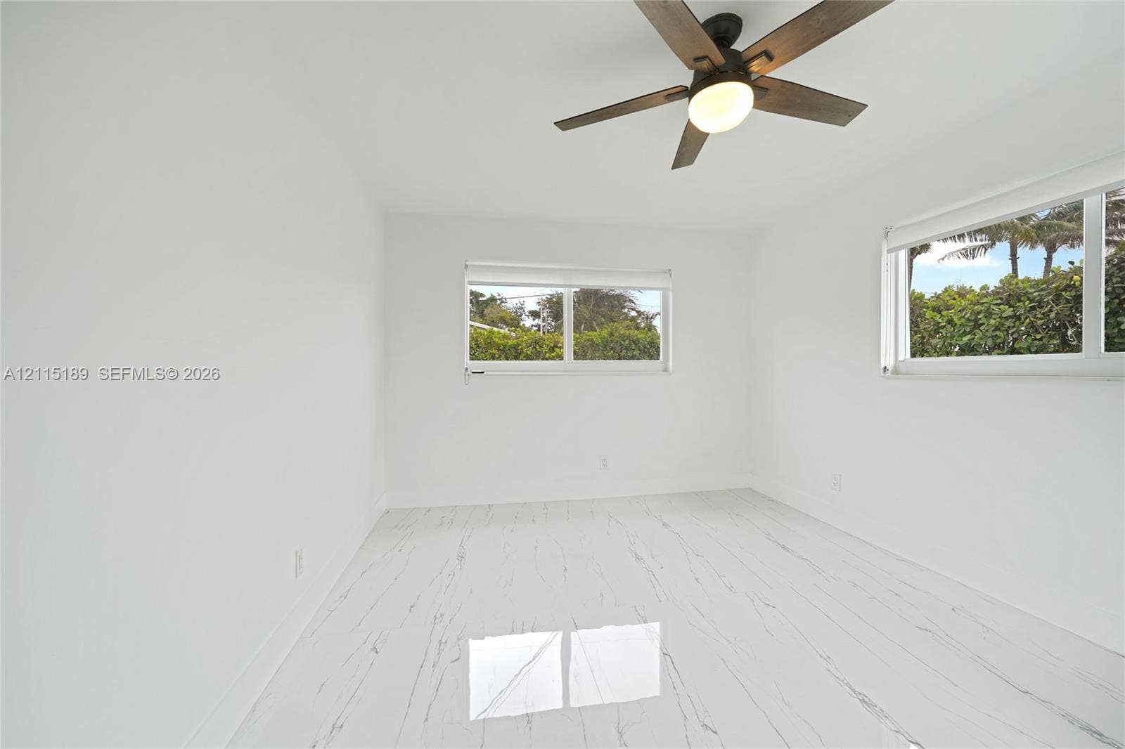 2111 N 14th Court, Hollywood, Hollywood, FL 33020 Light-filled interior featuring stone-finish flooring with veining, dual windows, and a dark-finish ceiling fan with integrated lighting