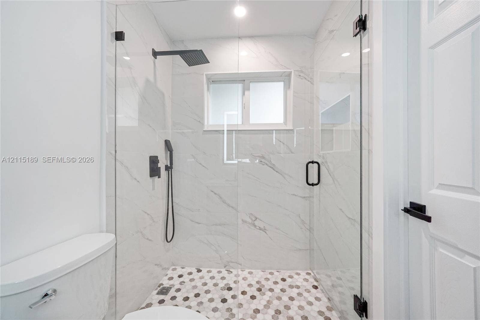 2111 N 14th Court, Hollywood, Hollywood, FL 33020 Walk-in shower featuring floor-to-ceiling stone-finish tile walls, hexagonal mosaic floor tile, frameless glass enclosure, and matte black plumbing fixtures