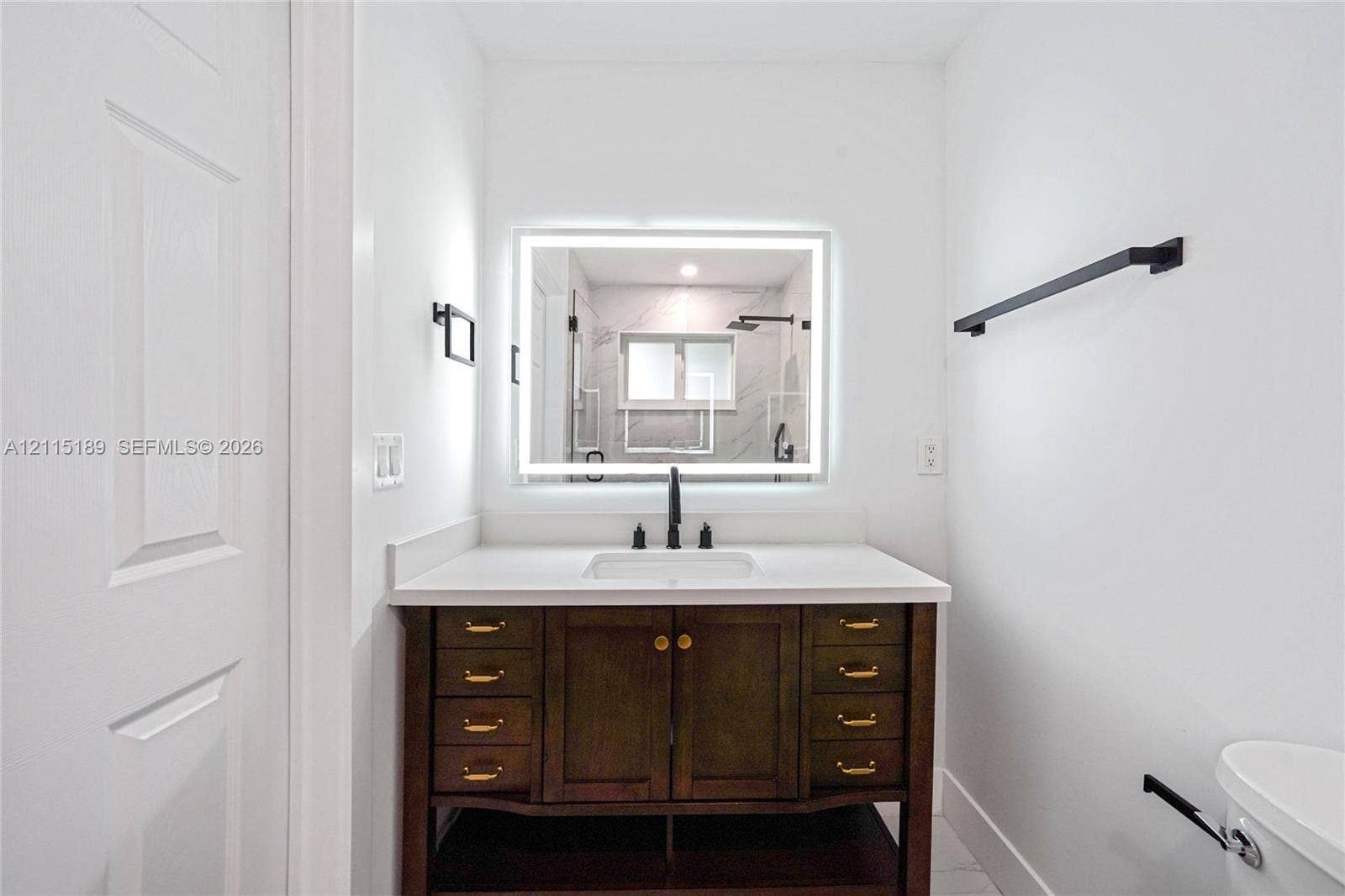 2111 N 14th Court, Hollywood, Hollywood, FL 33020 Bathroom vanity with a dark wood finish, white countertop with an integrated rectangular sink, matte black faucet, and backlit wall-mounted mirror, accented by matte black towel bars