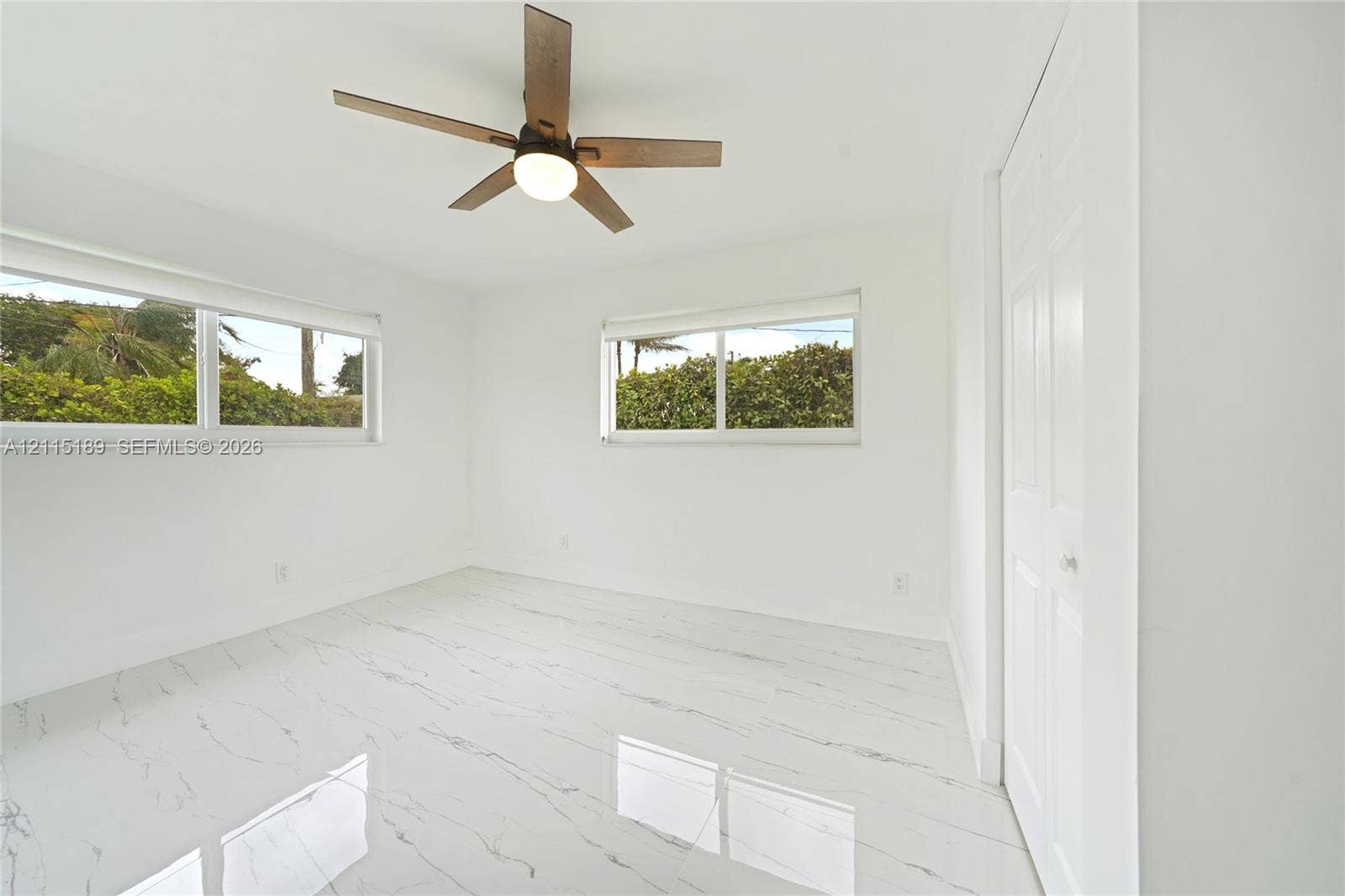 2111 N 14th Court, Hollywood, Hollywood, FL 33020 Interior space featuring large-format tile flooring with veining detail, multi-pane sliding windows, and a ceiling fan with integrated lighting