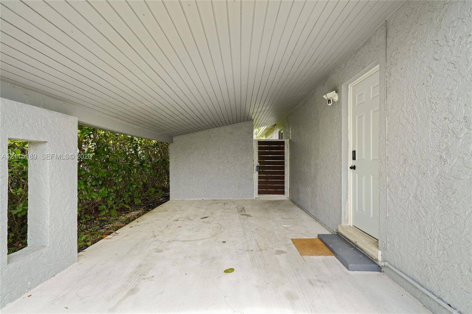 2111 N 14th Court, Hollywood, Hollywood, FL 33020 Covered carport featuring a concrete floor, textured stucco exterior walls, a beadboard-style ceiling, and a wooden slat privacy gate
